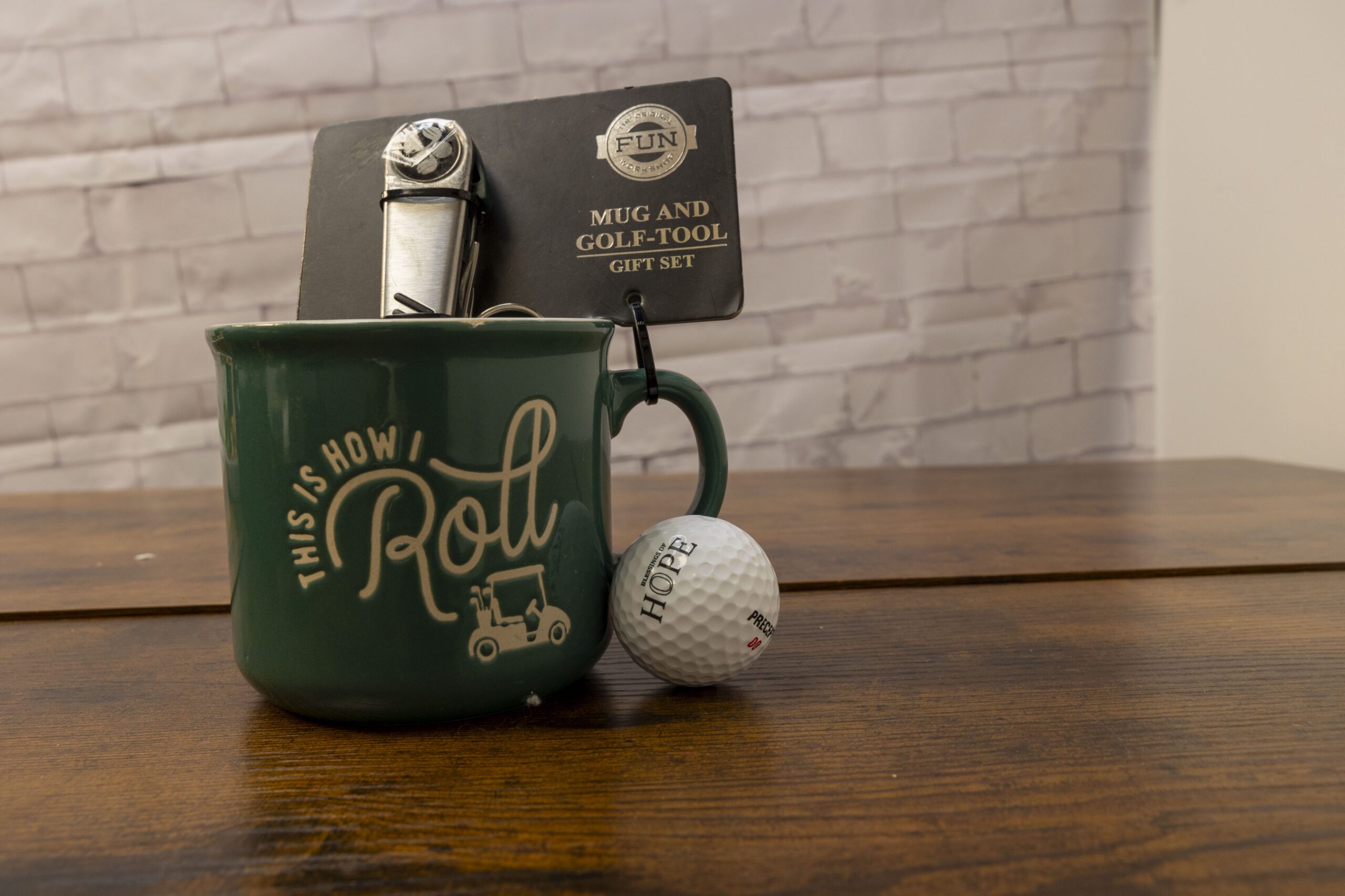 Green mug and golf tool gift set featuring the phrase "This is How I Roll," with a golf ball labeled "Hope" resting beside it, set against a wooden table.