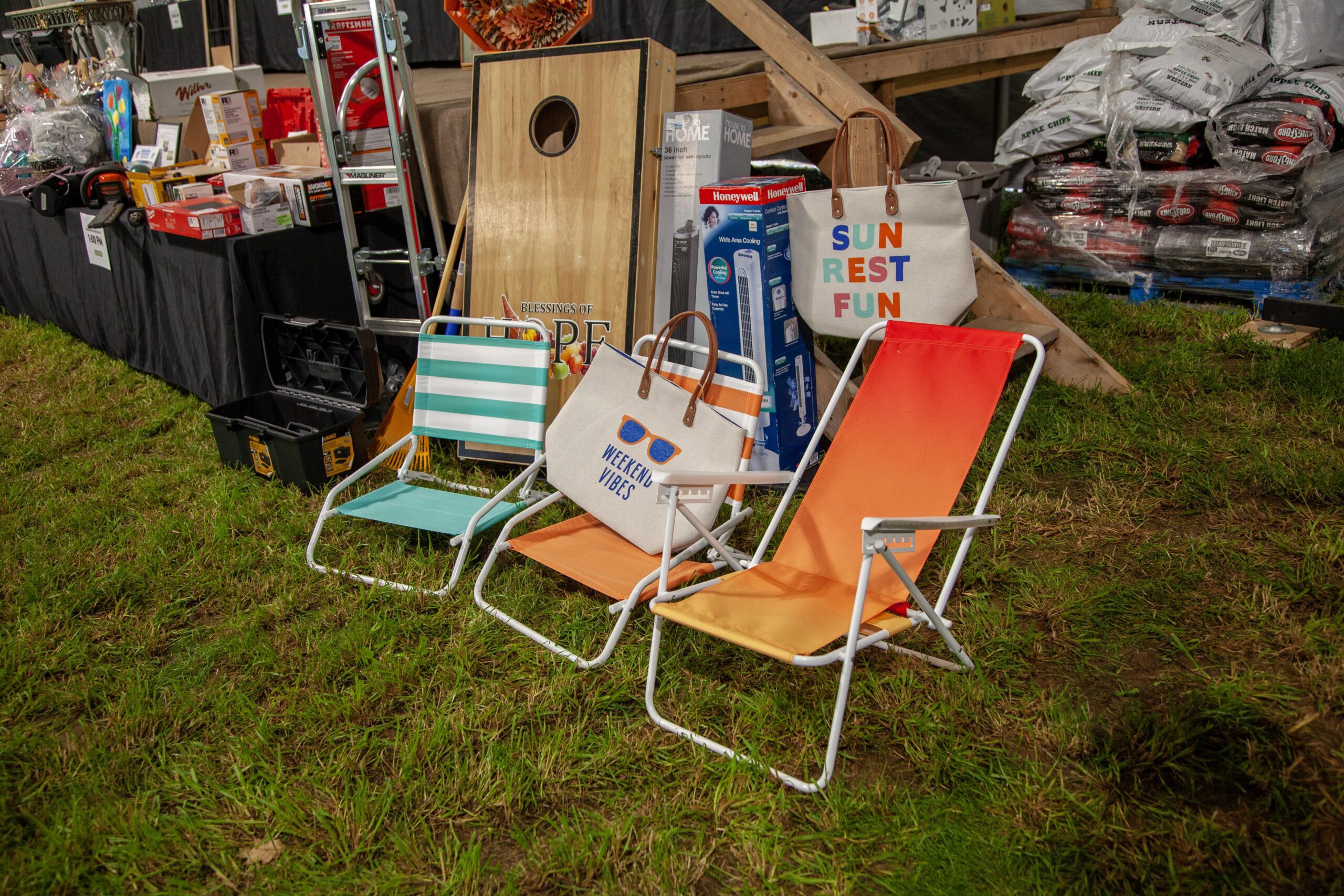 Colorful lawn chairs and tote bags displayed on grass, featuring the phrases "Weekend Vibes" and "Sun Rest Fun," alongside various outdoor and home products in a retail setting.