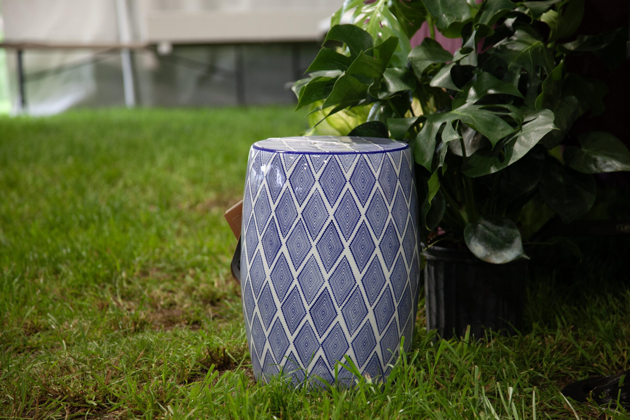 Blue and white patterned garden stool placed on green grass, accompanied by potted plants in the background, ideal for outdoor decor and seating.
