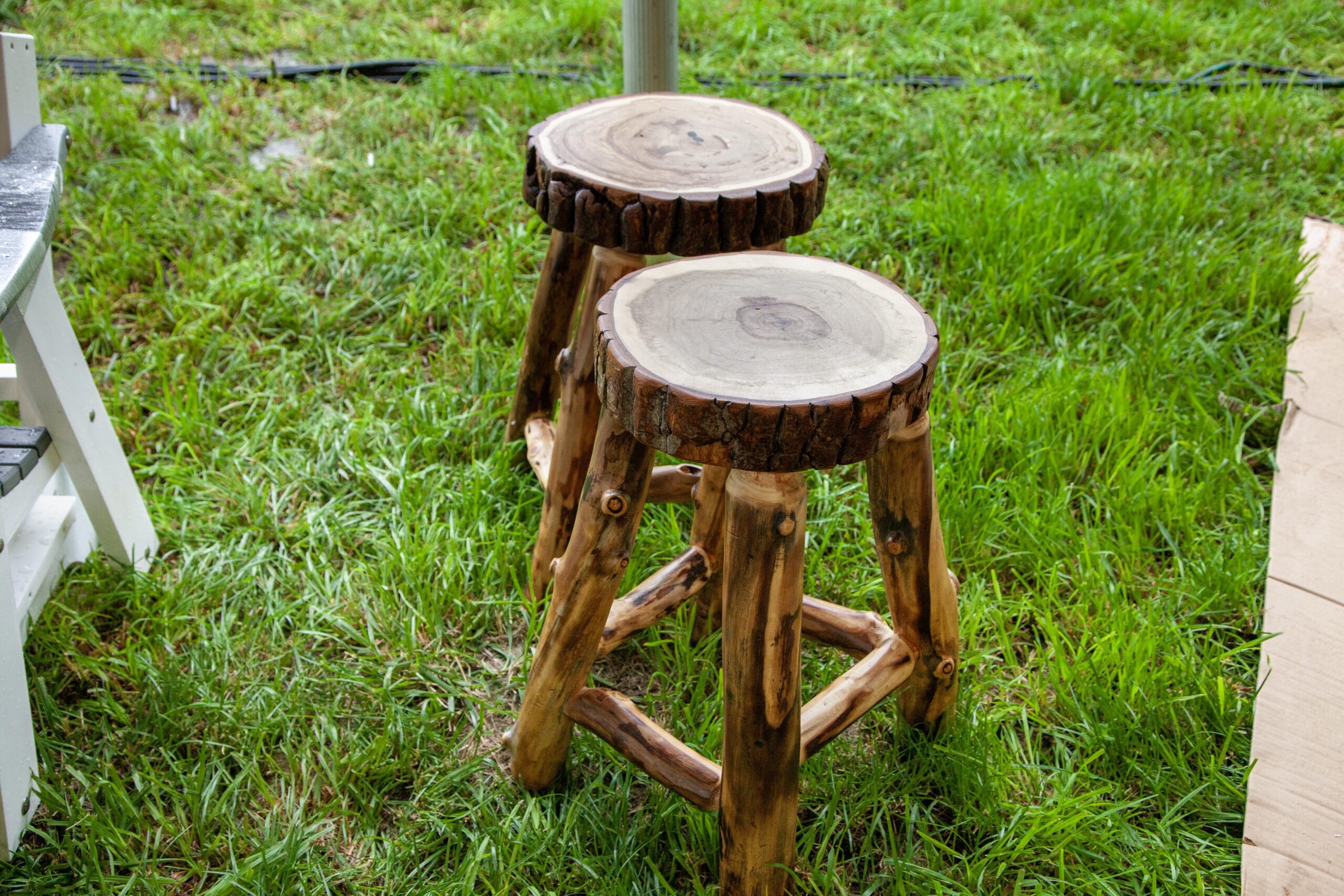 Rustic wooden stools made from natural logs, featuring round tops and sturdy legs, placed on green grass for outdoor seating.