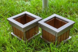 Two square wooden plant pots with gray trim sitting on green grass, ideal for gardening and home decor.