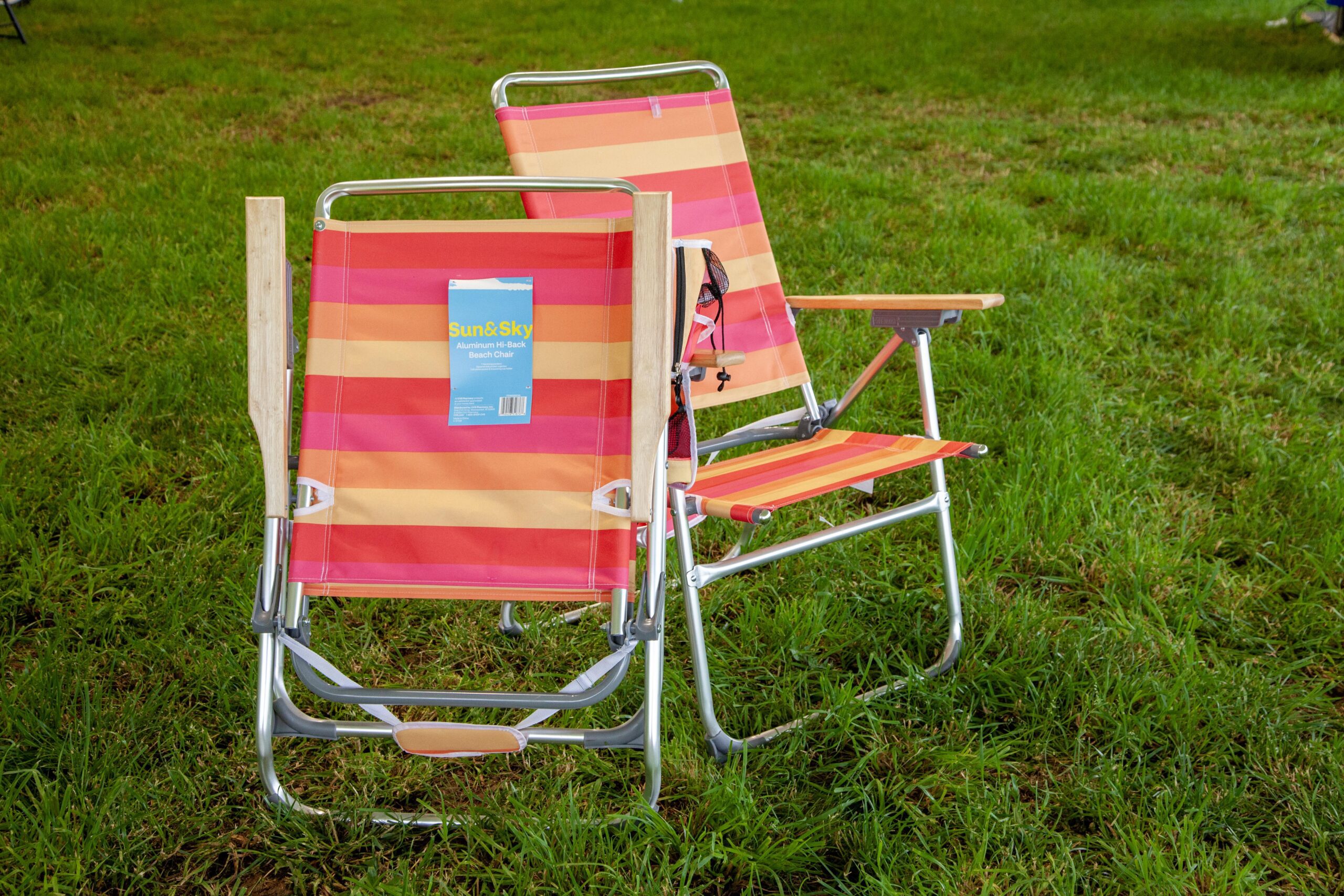 Two vibrant striped beach chairs, one with a tag displaying "Sun&Sky Aluminum Hi-Back Beach Chair," set on lush green grass, ideal for outdoor relaxation.