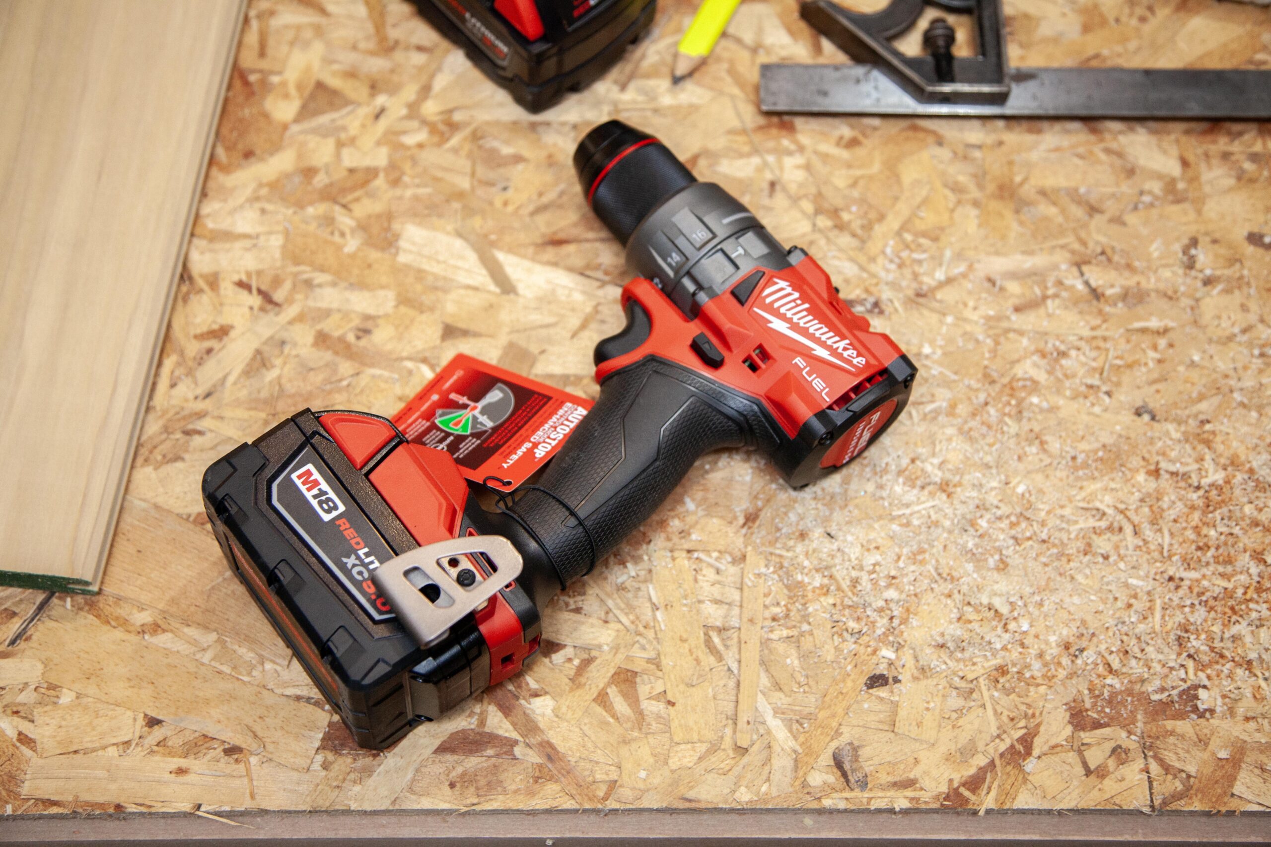 Milwaukee M18 Fuel cordless drill with battery on a wooden surface surrounded by sawdust and tools, highlighting durable construction for power tools enthusiasts.