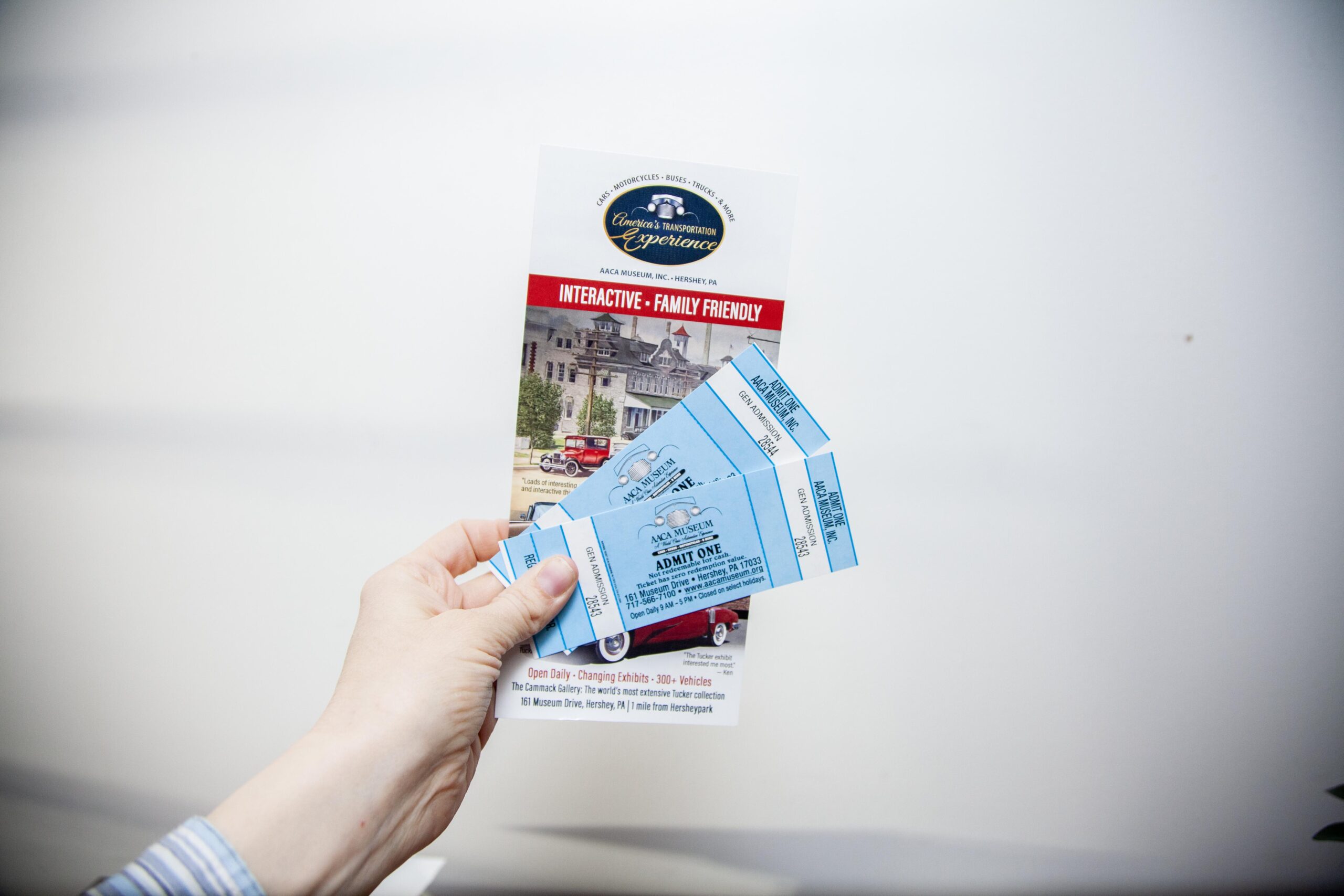 Hand holding a brochure and tickets for America's Transportation Experience, an interactive family-friendly museum in Hershey, Pennsylvania, featuring various vehicles and exhibits.