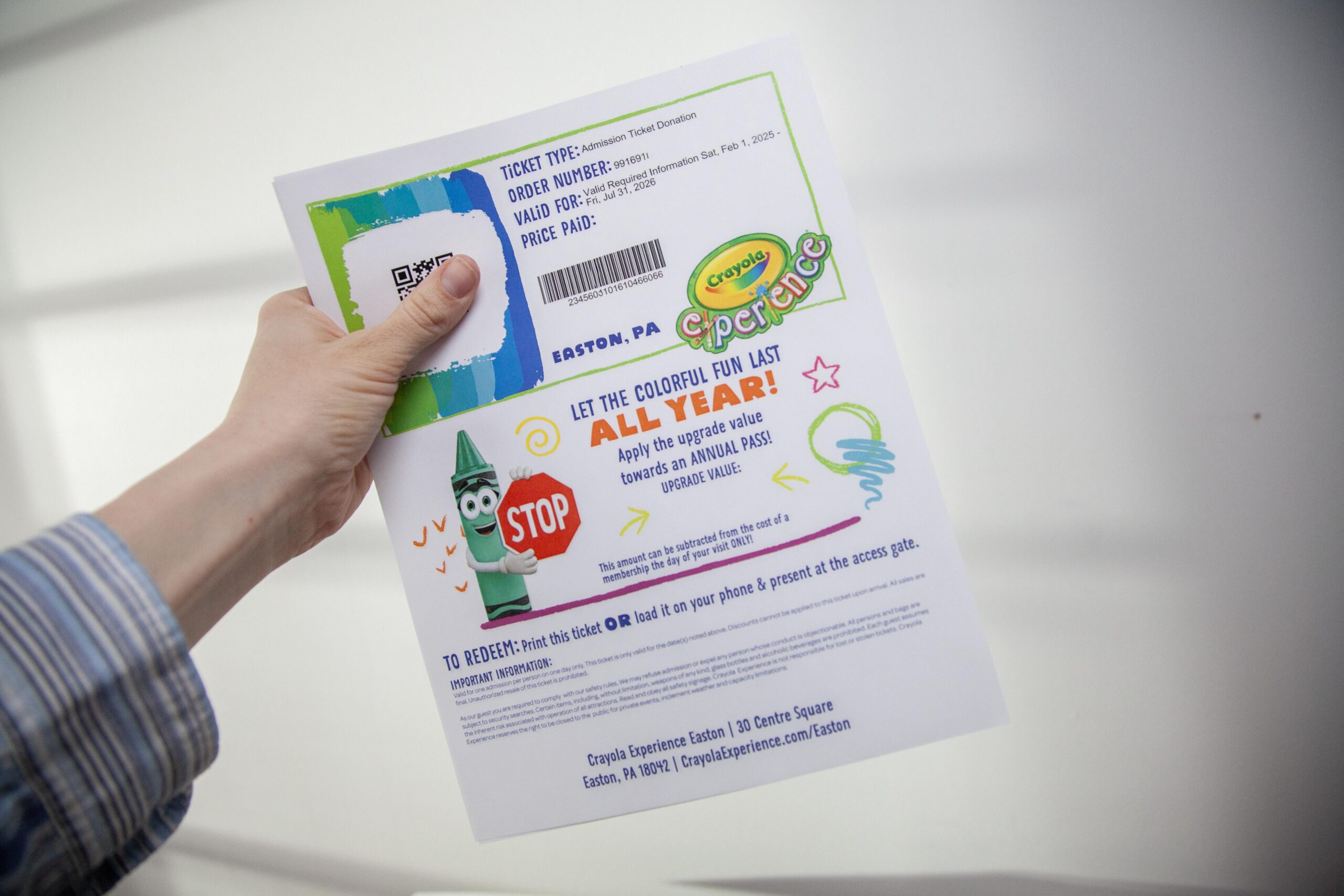 Hand holding Crayola Experience ticket with QR code and colorful design for Easton, PA location.