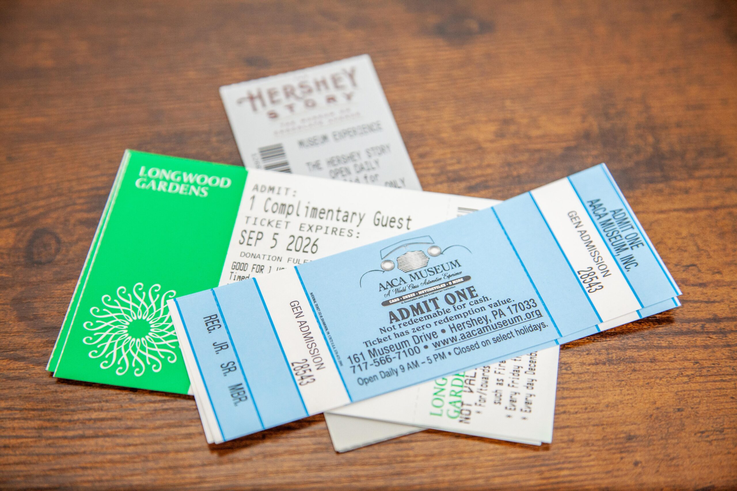 Collection of various attraction tickets including Longwood Gardens, The Hershey Story, and AACA Museum, laid out on a wooden table.
