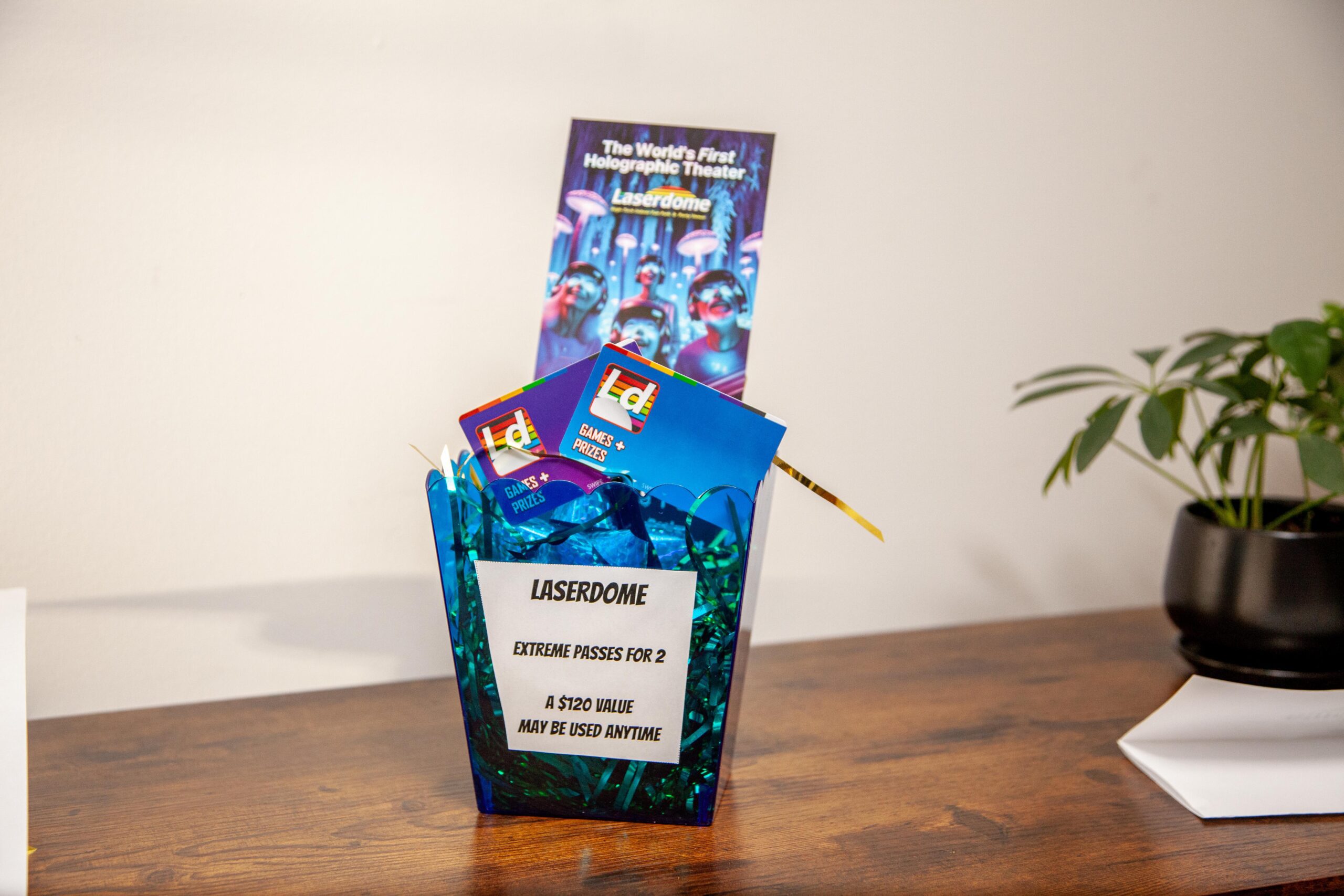 A display featuring a container with promotional materials for Laserdome, the world's first holographic theater, including extreme passes for two valued at $120, alongside a decorative background on a wooden surface.