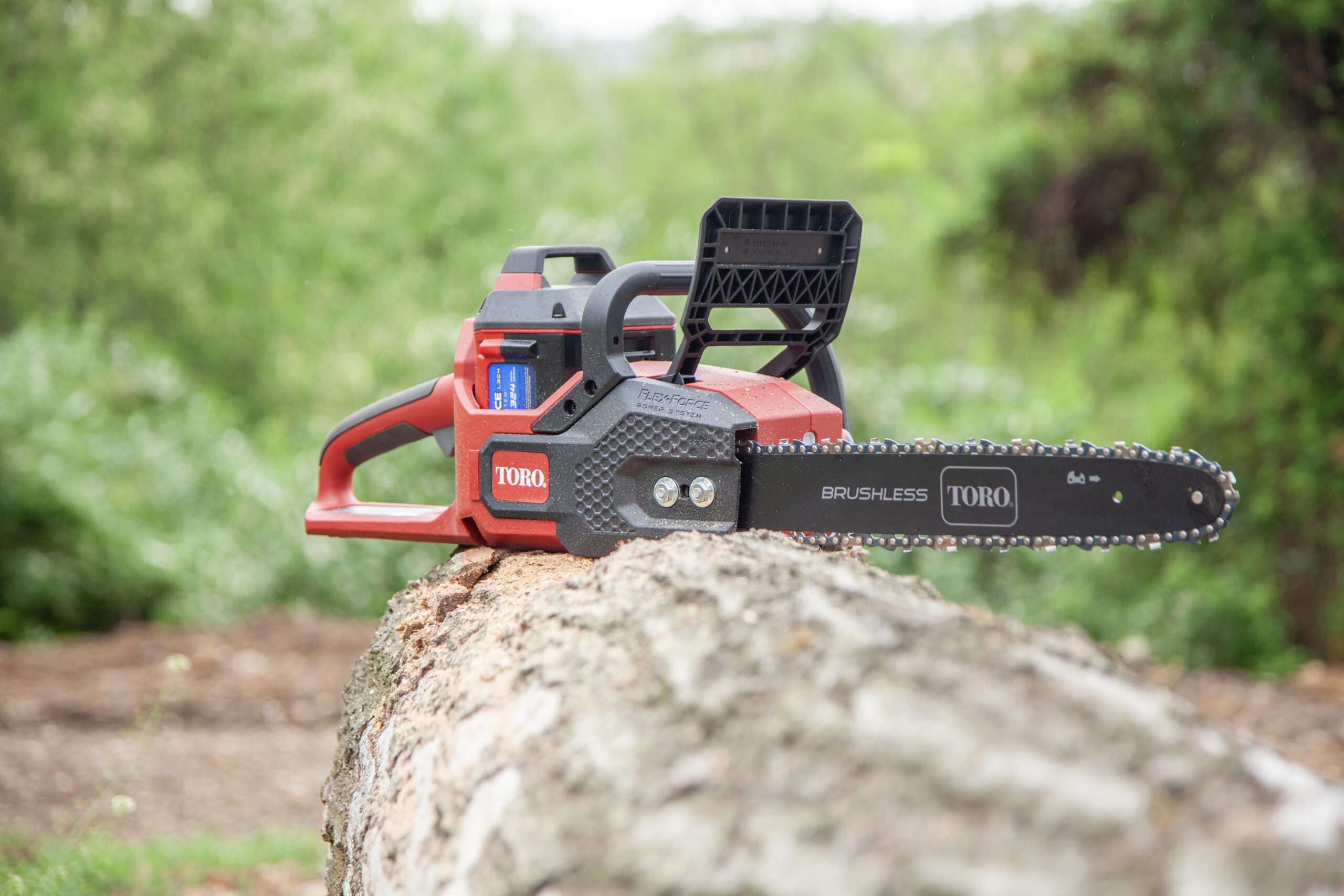 Toro brushless cordless chainsaw resting on a log in a green outdoor setting, showcasing its design and FlexForce power system for efficient cutting.