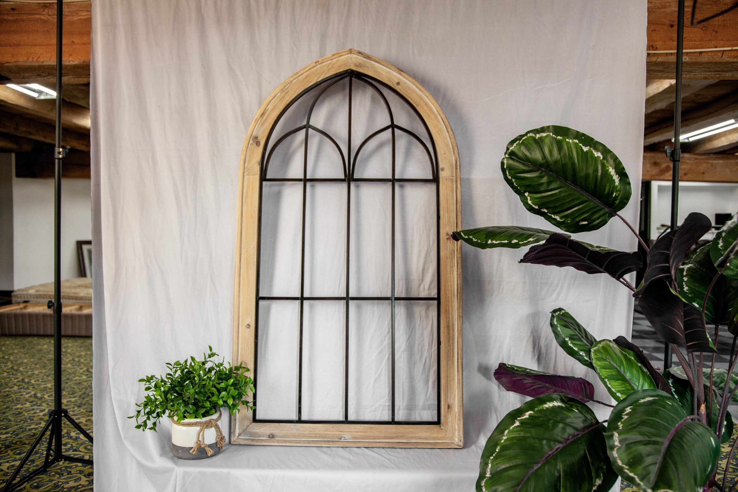 Rustic arched window frame displayed against a white backdrop, accompanied by a decorative potted plant, creating an inviting interior decor setting.