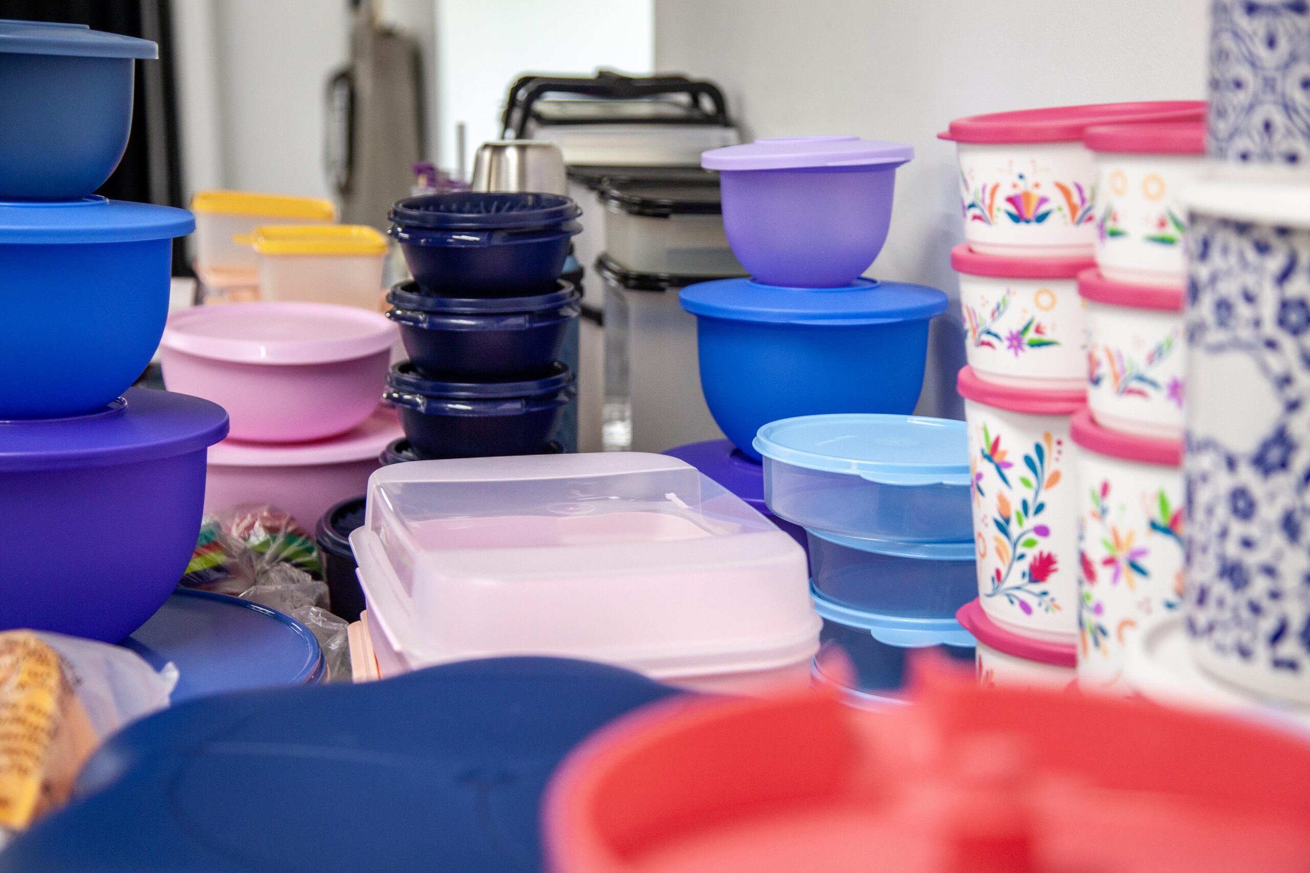 Colorful assortment of plastic storage containers in various sizes and shapes, highlighting blue, pink, and decorative designs, arranged on a countertop.