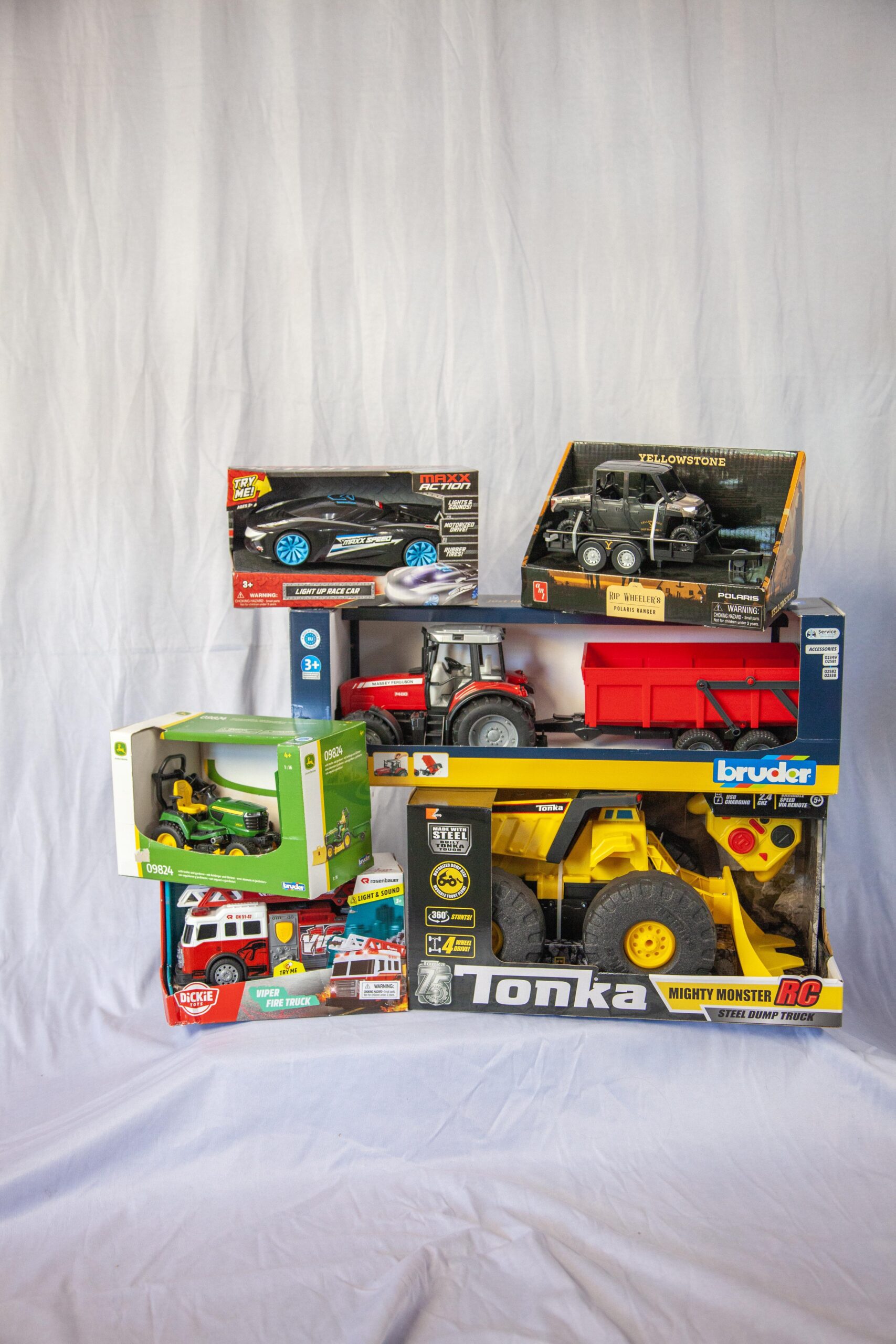 A collection of various boxed toy vehicles, including a light-up race car, a fire truck, a tractor, a dump truck, and an off-road utility vehicle, displayed against a plain white backdrop. Ideal for children's playtime and off-road adventures.
