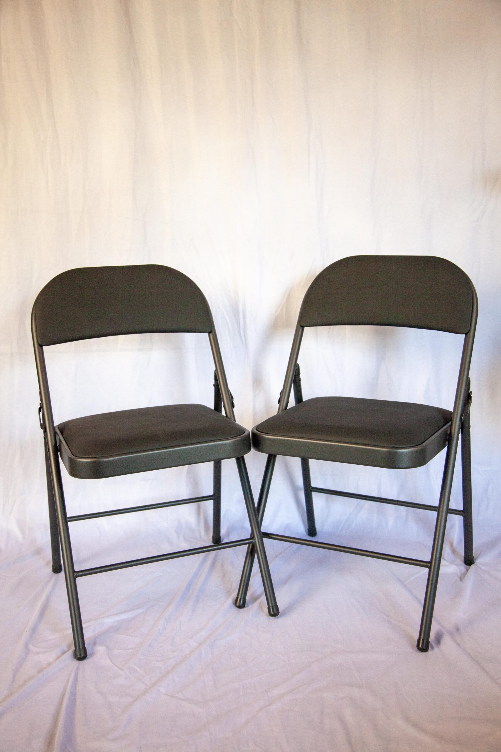 Two black folding chairs positioned on a light backdrop, showcasing their sleek design and sturdy construction, ideal for events and gatherings.