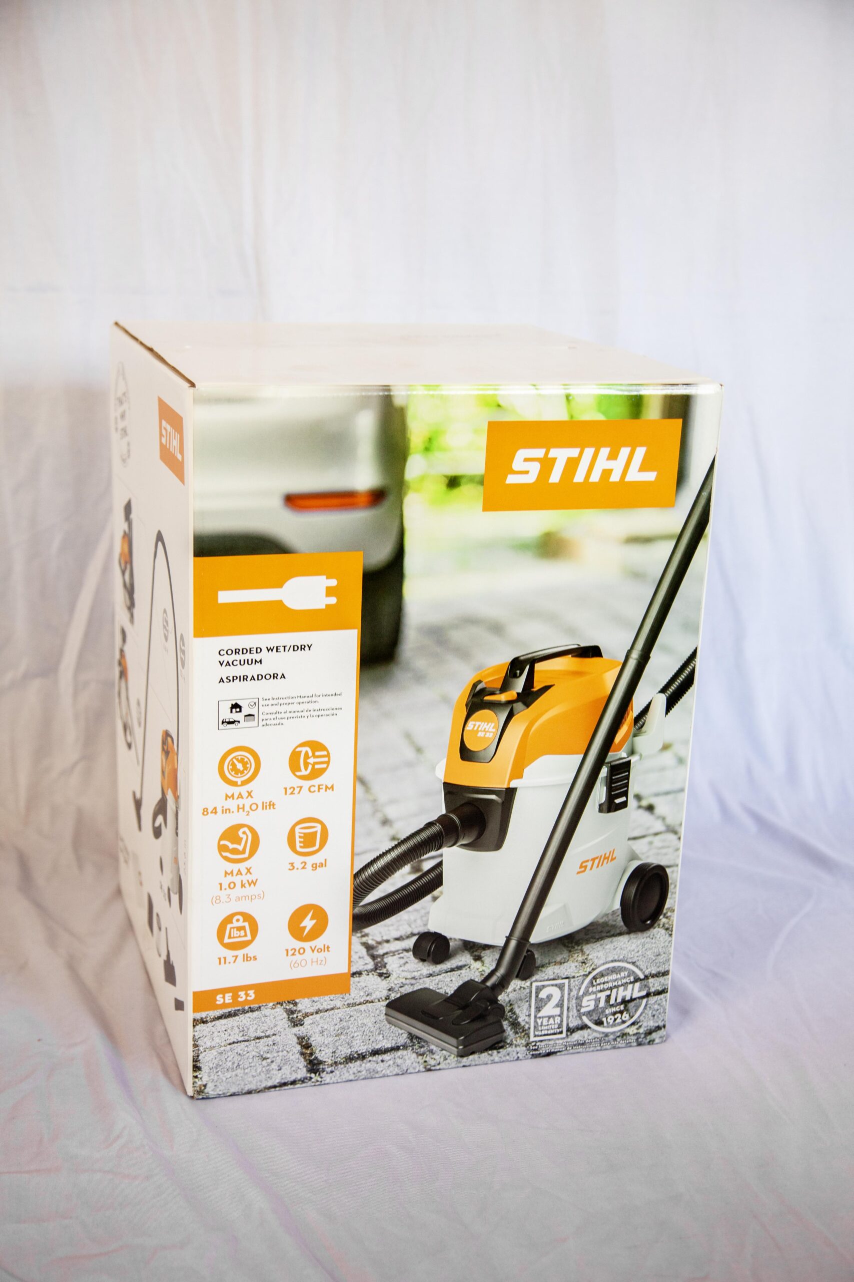 Corded wet/dry vacuum cleaner from STIHL, model SE 33, featuring a maximum lift of 84 inches and airflow of 127 CFM. The vacuum has a 3.2-gallon capacity, operates at 1.0 kW (8.3 amps), and is designed for easy transport with a weight of 11.7 lbs. Suitable for various cleaning tasks, showcasing product specifications and branding on the packaging.