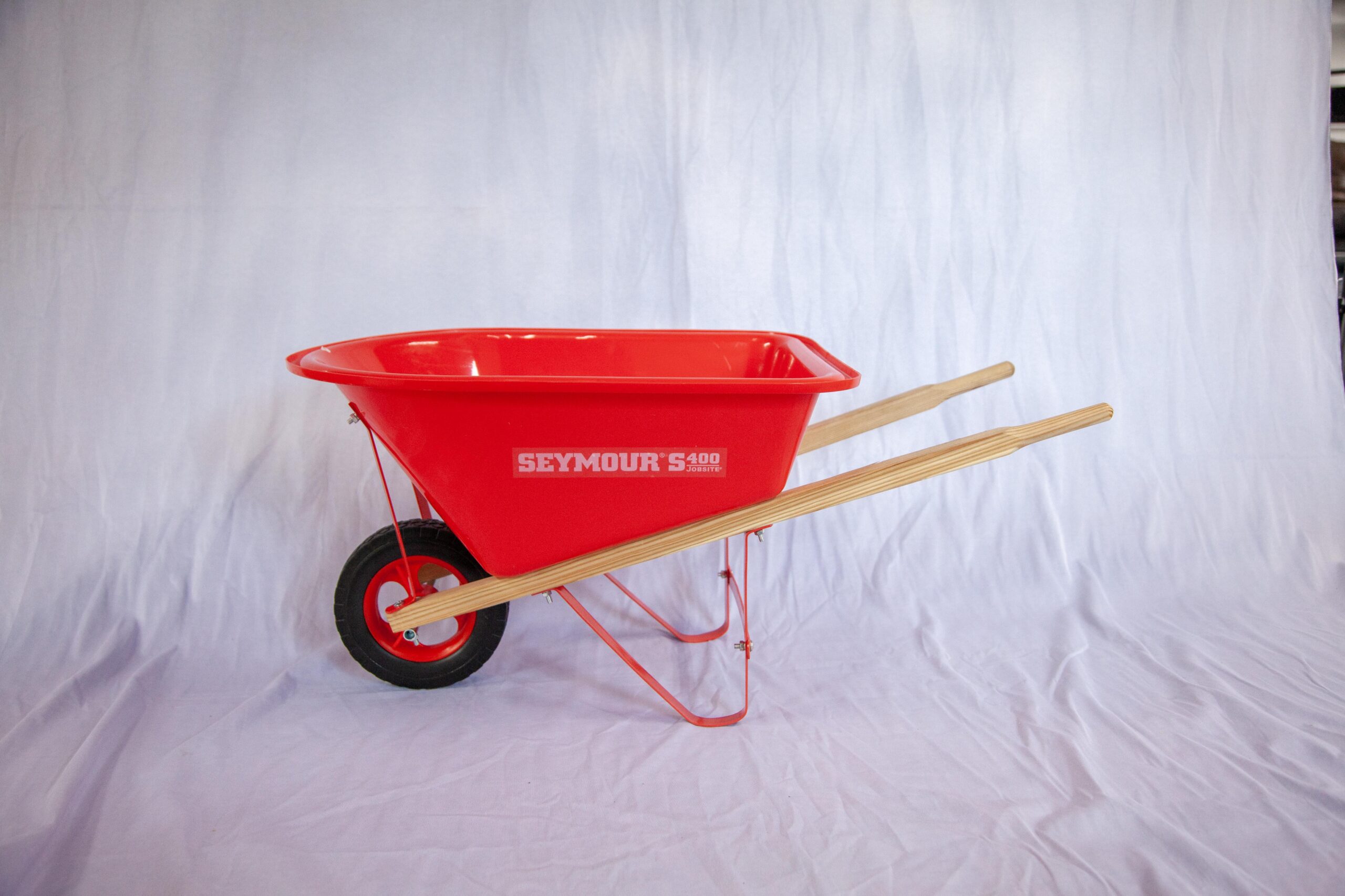Bright red Seymour S400 wheelbarrow features a sturdy wooden handle and a reliable rubber wheel, ideal for landscaping and gardening tasks.