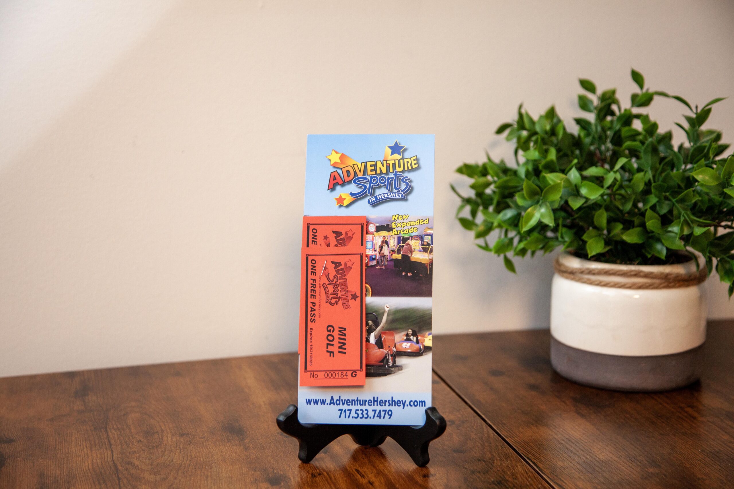 Adventure Sports flyer on wooden table near green plant, featuring mini golf and arcade promotion.