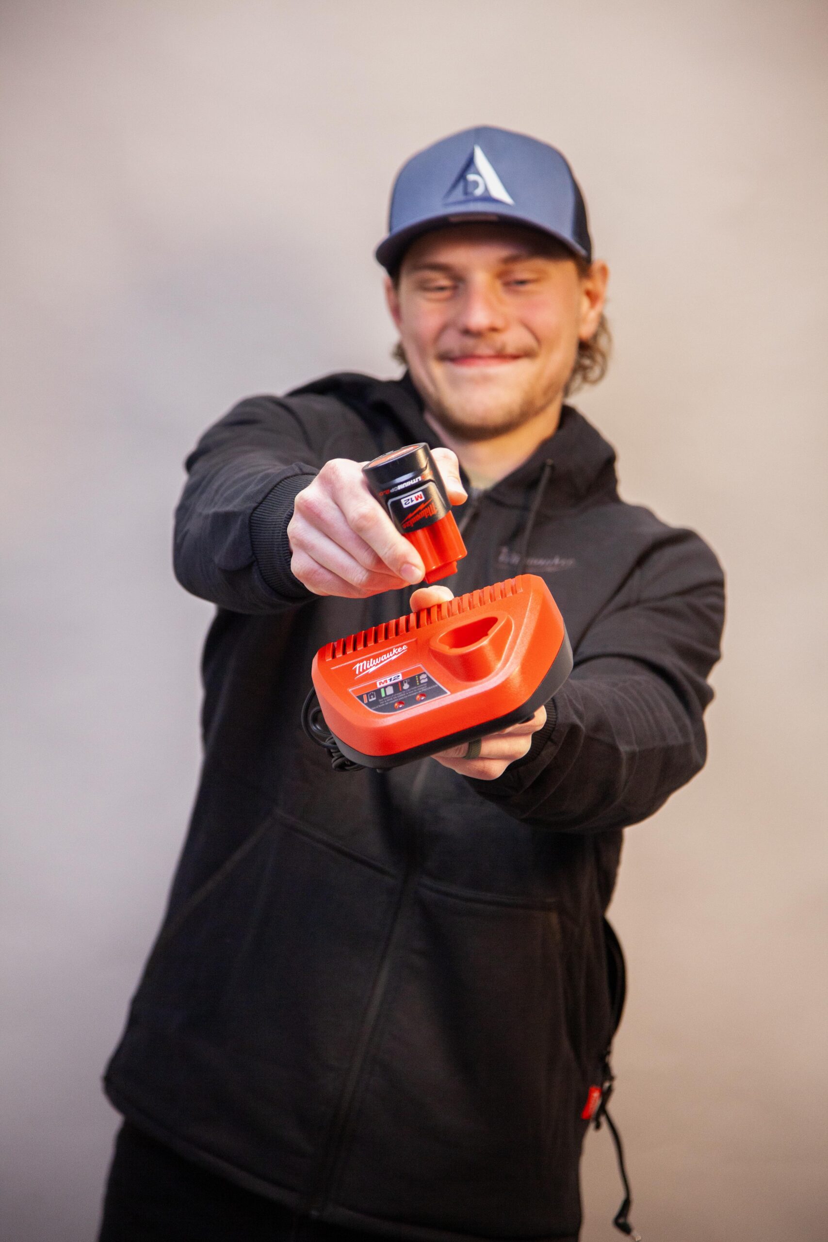 Man holding Milwaukee battery and charger, demonstrating tool charging process.