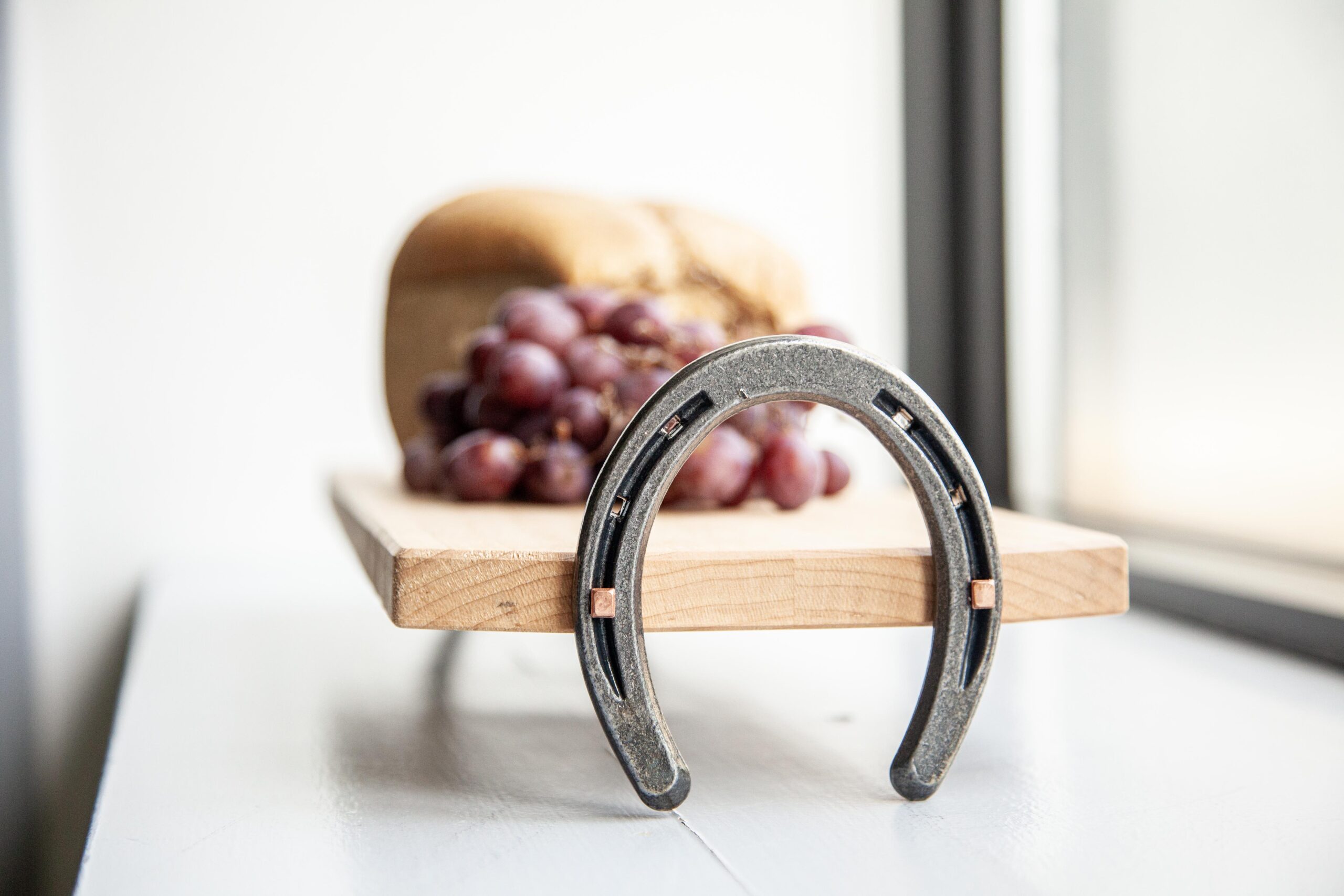 Horseshoe and grapes on wooden board with bread. Symbol of luck and abundance by a bright window.