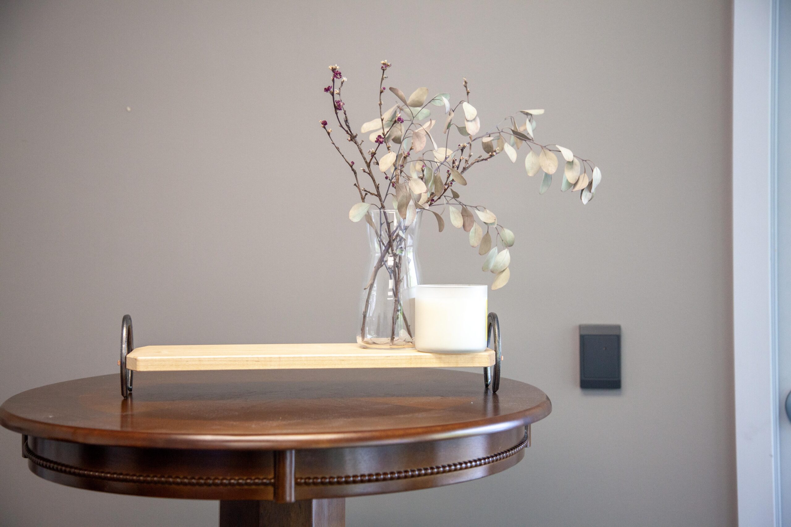 Minimalist decor with a vase of dried branches and a candle on a wooden table against a neutral wall.