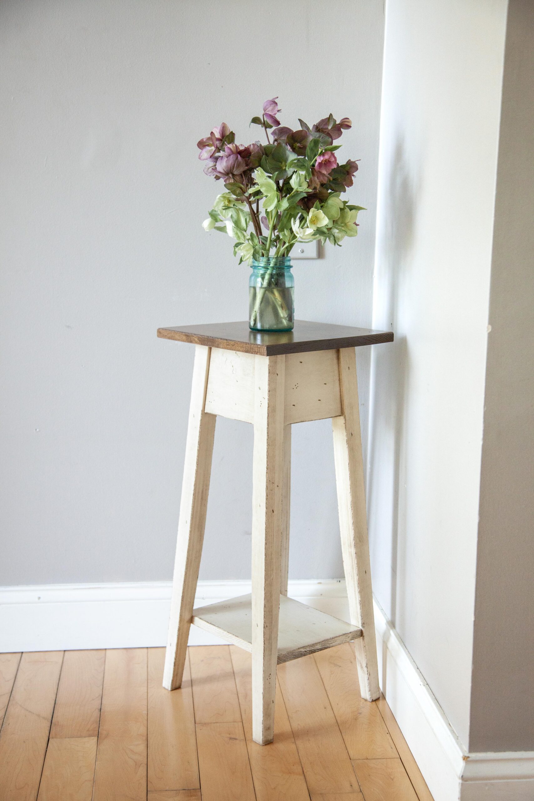 Vibrant flowers in a blue jar on a small white table against a gray wall, simple and elegant home decor.