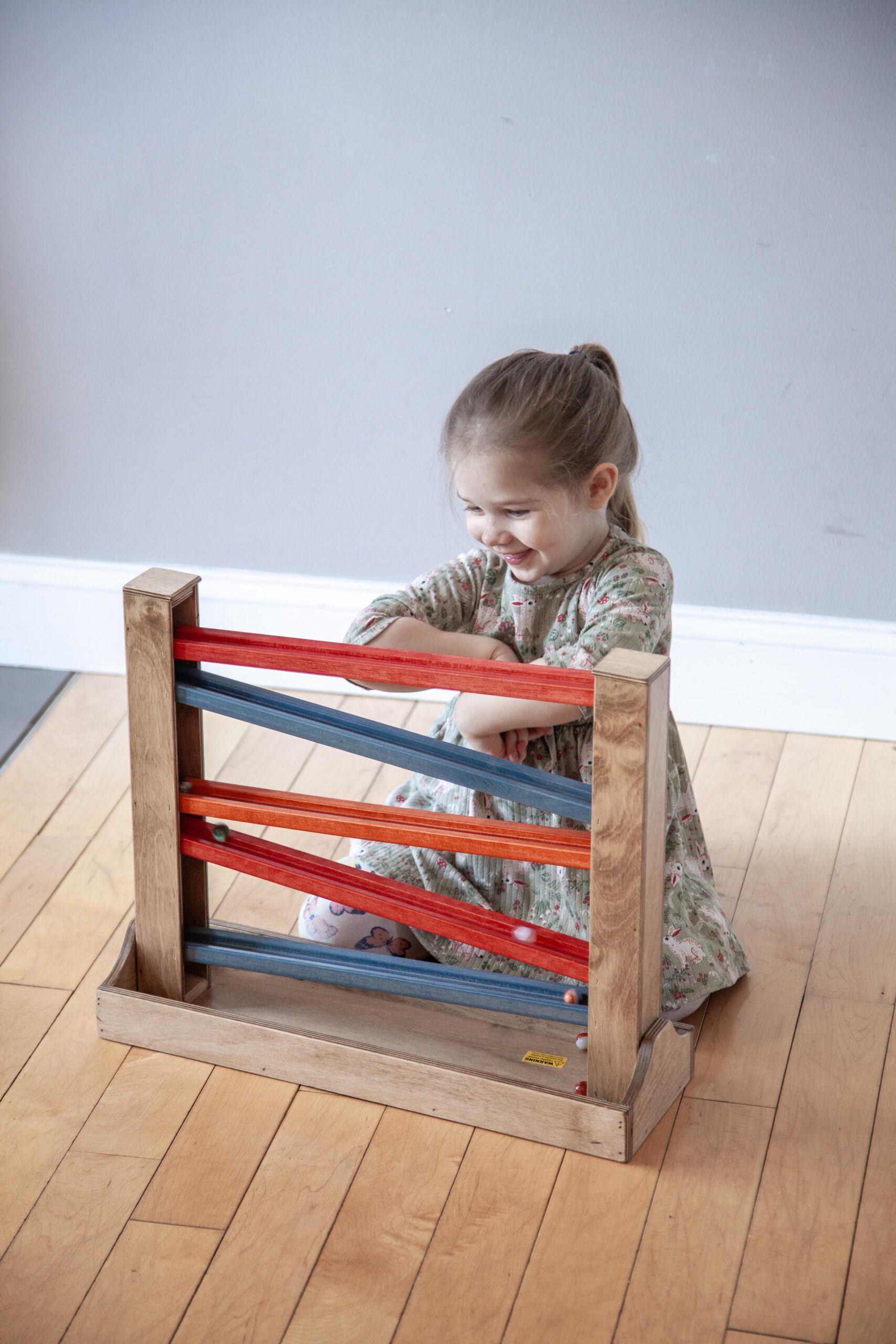 Child playing with a colorful wooden marble run on the floor, smiling with joy.