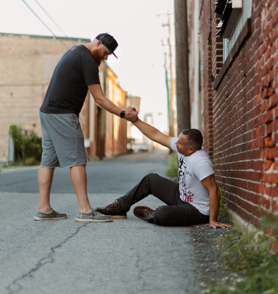 Two men in a friendly handshake, one helping the other get up in a brick alleyway.