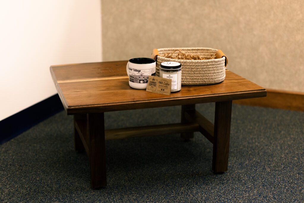 Wooden coffee table with decorative items including a ceramic mug, a candle, and a woven basket, set against a neutral wall and carpeted floor. Ideal for home decor inspiration and cozy living spaces.