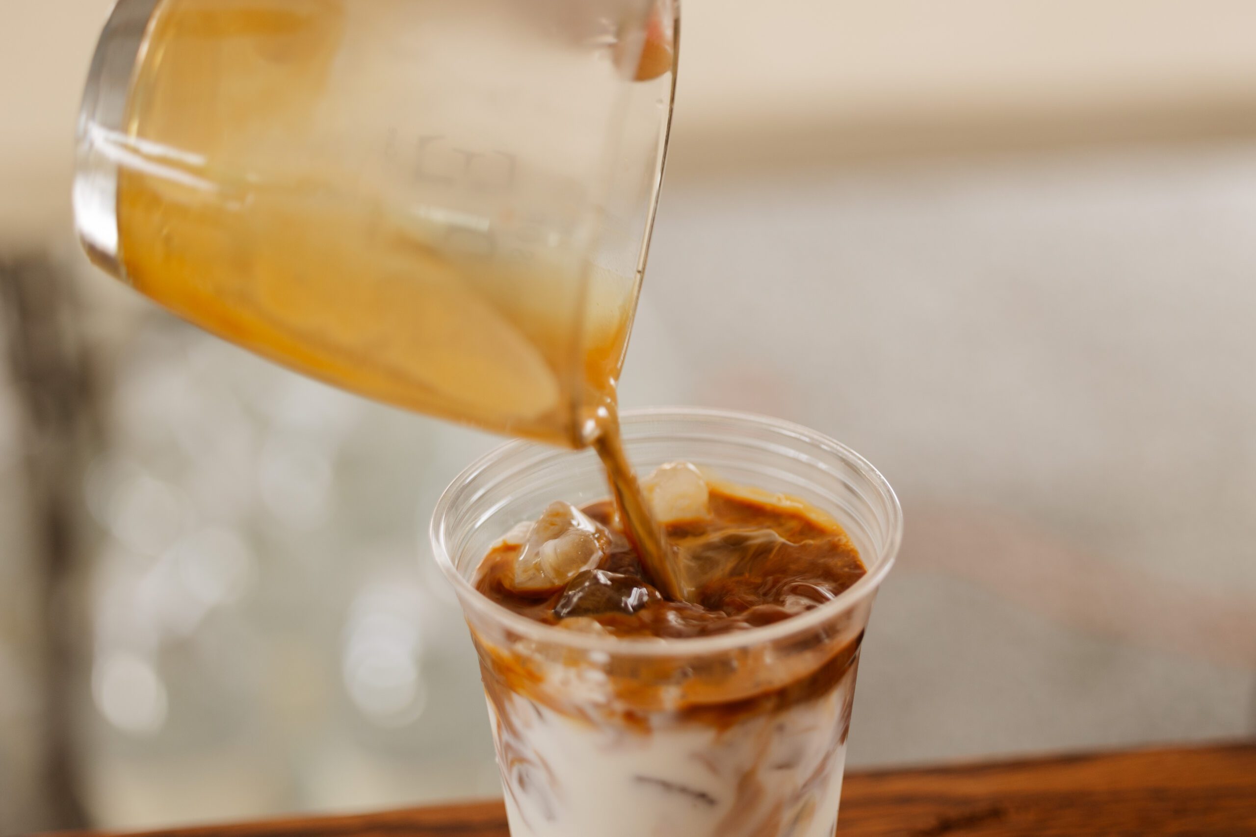 A close-up of a glass being poured with iced coffee, showcasing a swirl of rich brown coffee mixing with creamy milk and ice cubes.