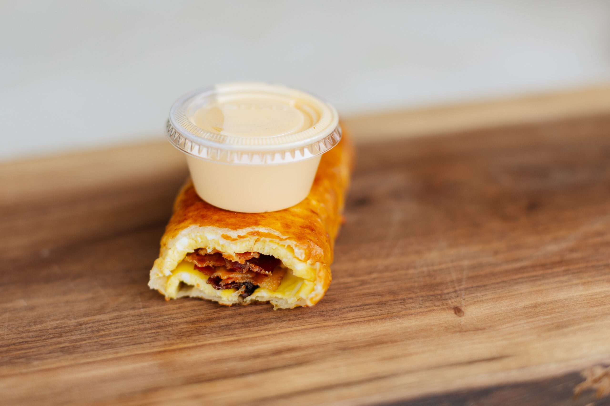 Savory pastry filled with bacon and cheese on a wooden surface, topped with a small container of creamy sauce.