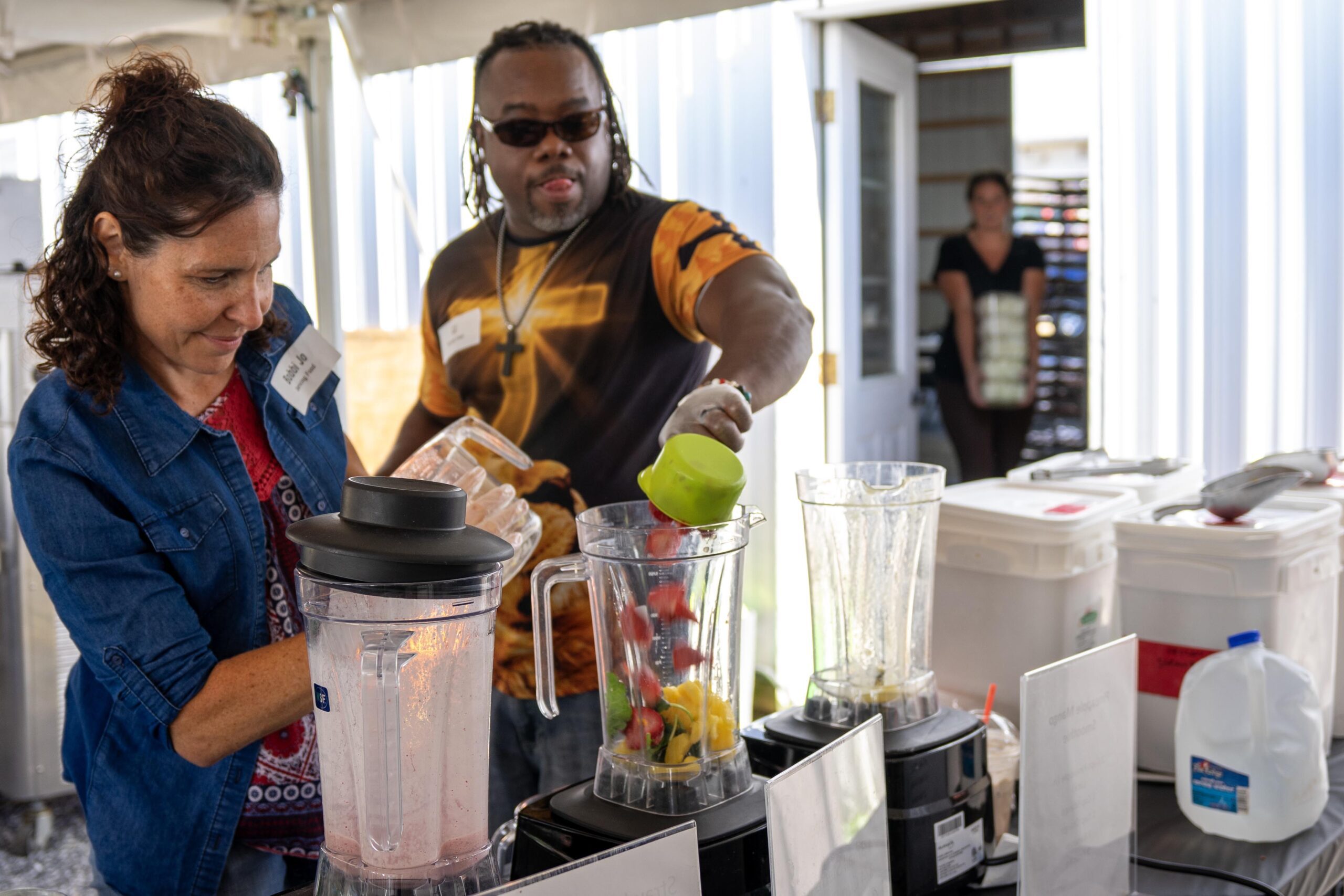 Participants at a smoothie-making workshop prepare fresh fruit in blenders, showcasing teamwork and culinary skills in a lively outdoor setting.