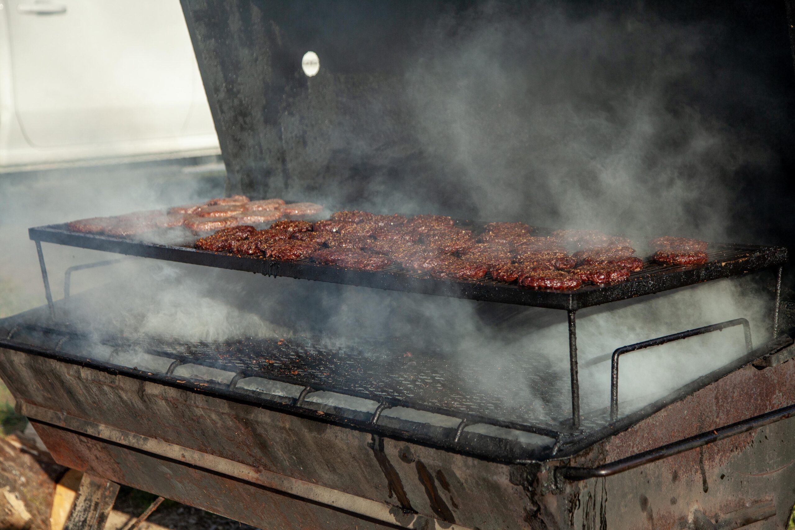 Close-up of burgers grilling on a smoky barbecue, showcasing sizzling meat and a charcoal grill setup. Ideal for outdoor cooking and BBQ enthusiasts looking for grilling inspiration.