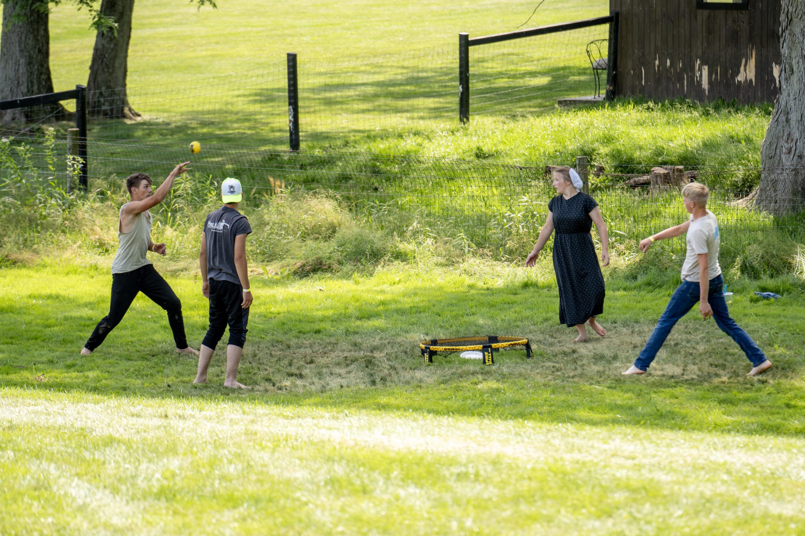 Group of young people playing catch outdoors on a sunny day in a grassy field, with a yellow and black spikeball net in the foreground. They appear to be enjoying a recreational activity, showcasing a sense of community and outdoor fun.