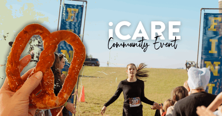 Alt text: A vibrant scene from the iCARE community event featuring a close-up of a soft pretzel in the foreground, while in the background, a young female runner crosses the finish line amidst cheering spectators. Colorful banners mark the event, highlighting community spirit and participation.