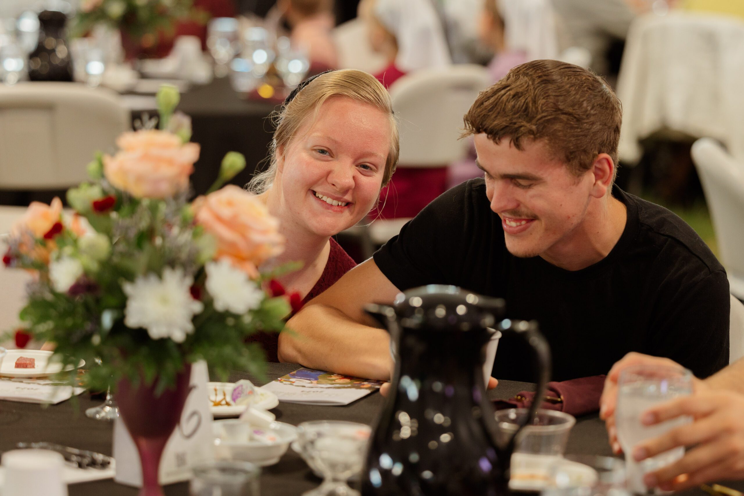 Couple sharing a joyful moment at a dining table adorned with flowers and tableware, smiling and engaging in conversation during a social event.