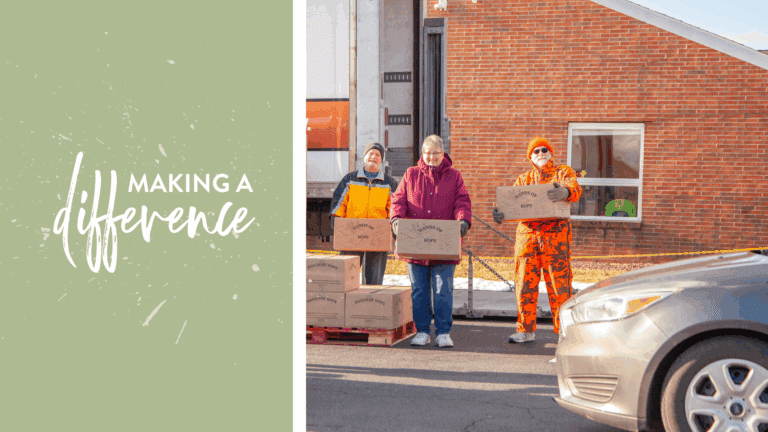 Three volunteers stand outside a building, each holding boxes labeled "Hands of Hope," as they participate in a community food distribution effort. The scene reflects their commitment to making a difference in the lives of those in need.