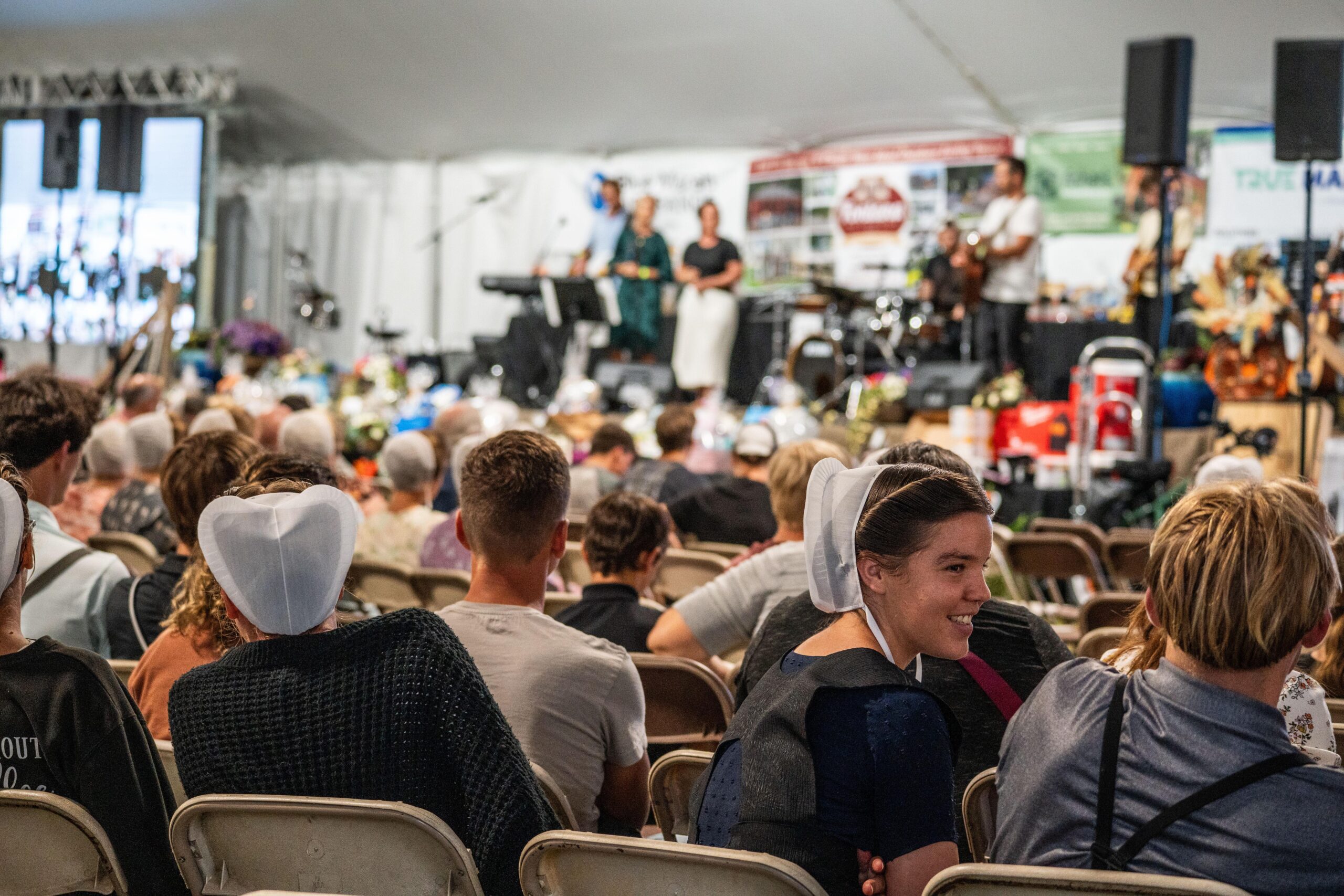 Audience enjoying a live music performance at a community event under a large tent, featuring people in traditional attire and musicians on stage.