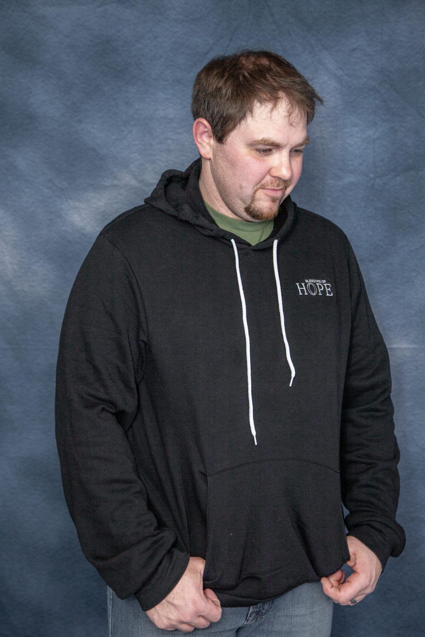 Man wearing a black hoodie with a front pocket and white drawstrings, standing against a blue background. The hoodie features the word "HOPE" embroidered on the chest.