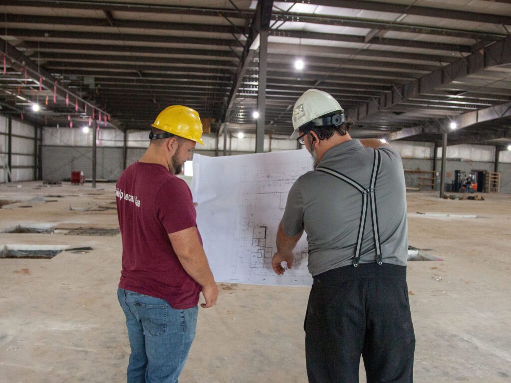 Construction workers examining blueprints inside a large industrial building, showcasing teamwork and planning in a construction site.