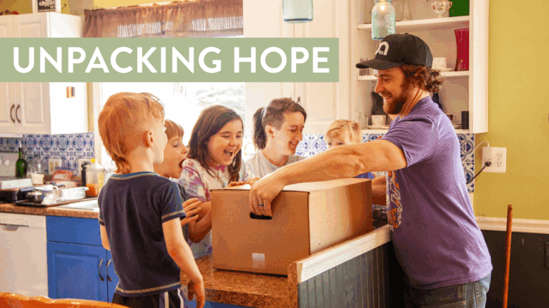 A man and several children excitedly gather around a kitchen counter as he prepares to open a large cardboard box, symbolizing joy and community engagement. The scene captures the essence of hope and togetherness in a warm, inviting home setting.