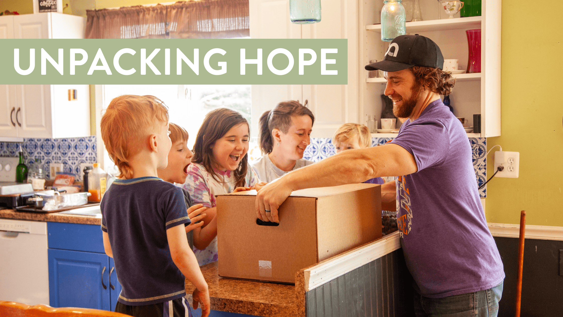 A man and several children excitedly gather around a kitchen counter as he prepares to open a large cardboard box, symbolizing joy and community engagement. The scene captures the essence of hope and togetherness in a warm, inviting home setting.