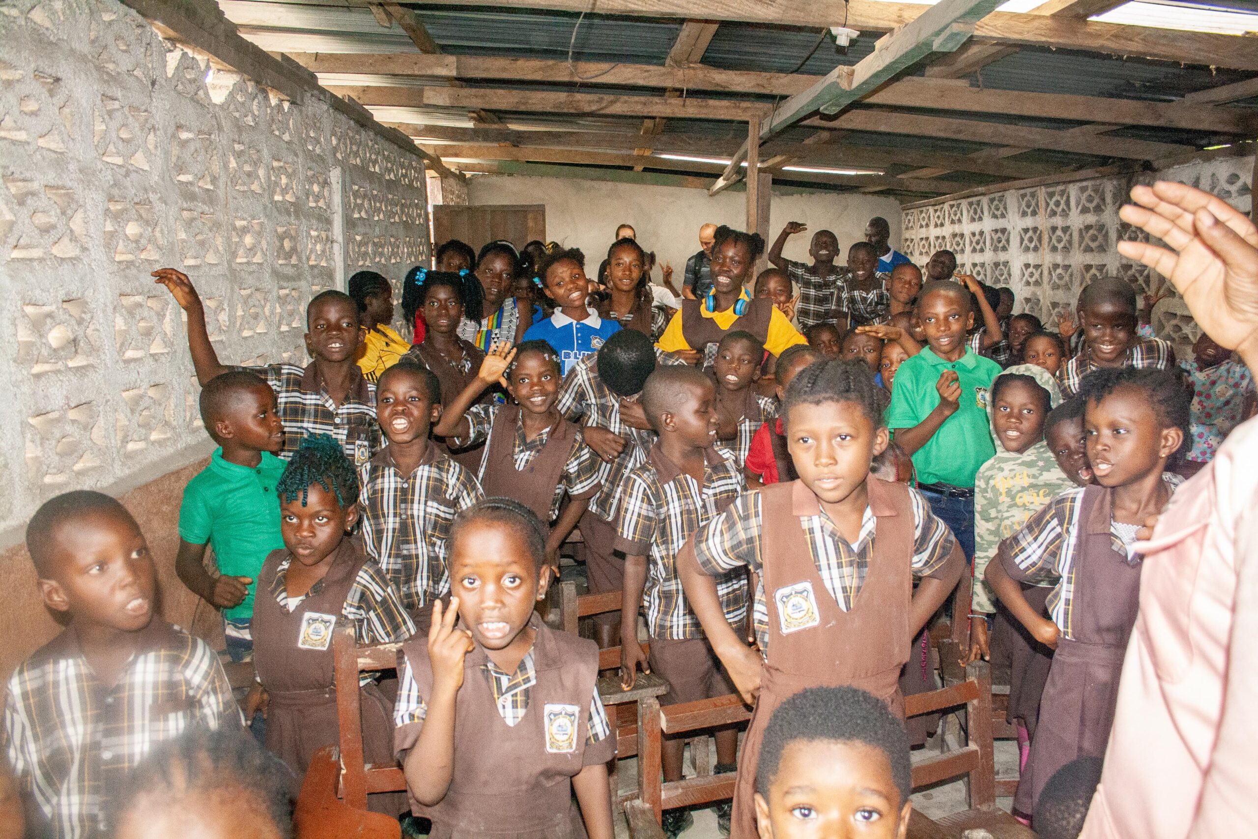 A lively classroom filled with young children in school uniforms, engaged and smiling, showcasing a vibrant learning environment. The room is filled with students interacting and participating enthusiastically, highlighting the importance of education and community involvement.