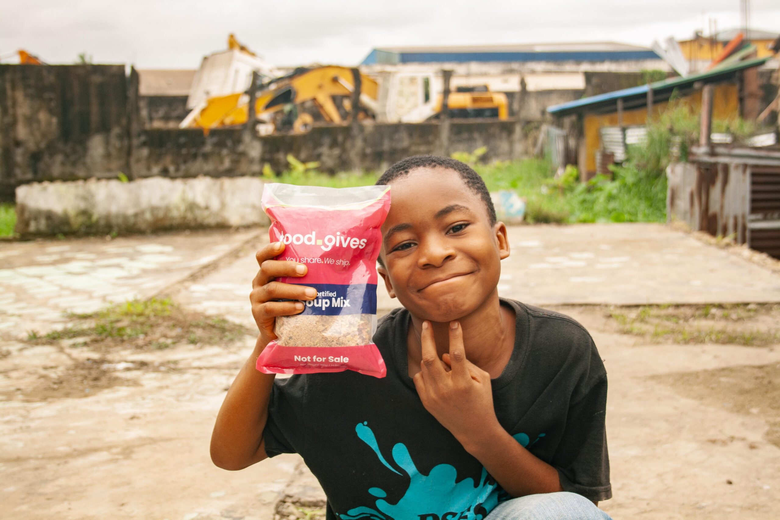 Young boy smiling while holding a bag of Food Gives certified soup mix, showcasing support for food distribution initiatives in a community setting.