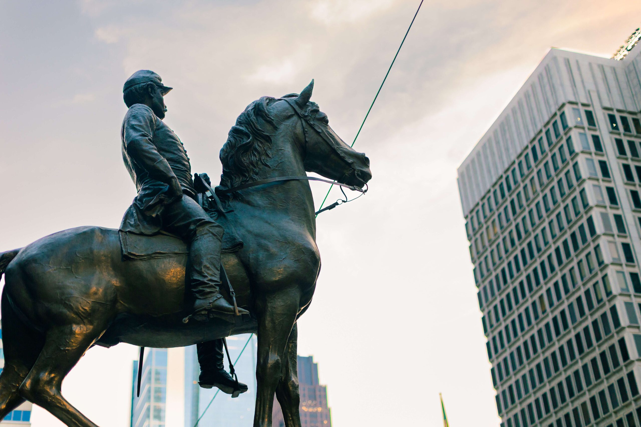 Statue of a mounted soldier in historical military attire, set against a backdrop of modern skyscrapers, showcasing the contrast between historical and contemporary architecture.