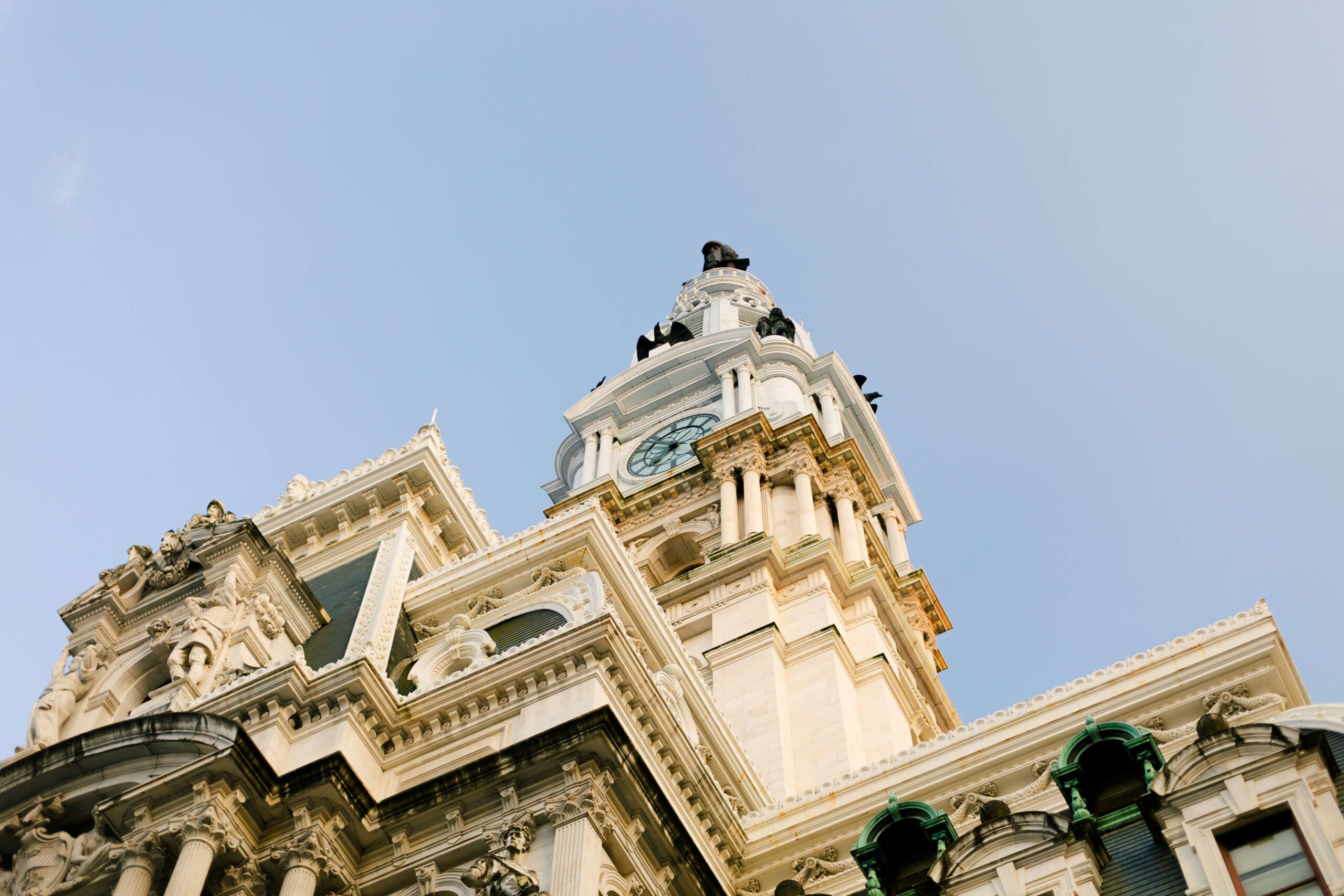 Historic clock tower with intricate architectural details against a clear blue sky. The image showcases ornate sculptures and decorative elements on the building's facade, highlighting its historical significance and craftsmanship.