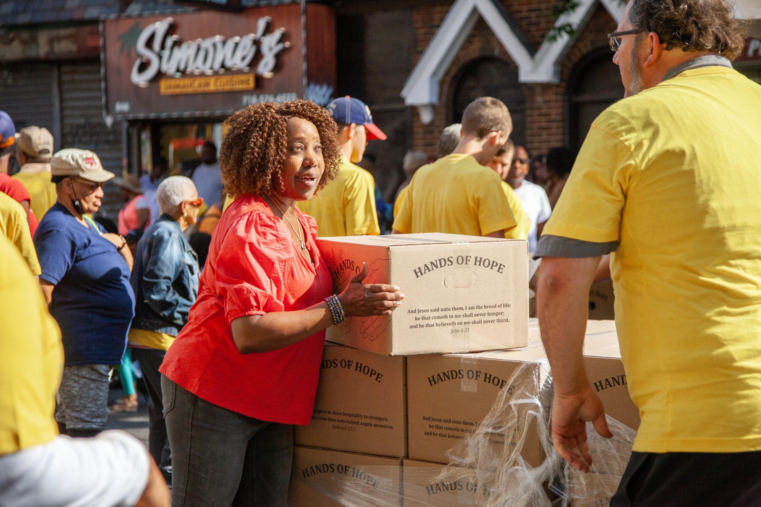 Community volunteers distribute food boxes labeled "Hands of Hope" during an outreach event, promoting support and solidarity in a vibrant urban setting.