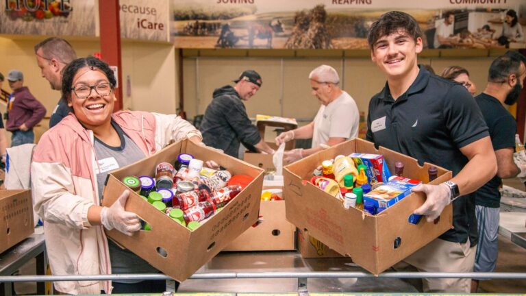 Volunteers smiling while sorting food items in a community food pantry, showcasing teamwork and community support in addressing food insecurity.