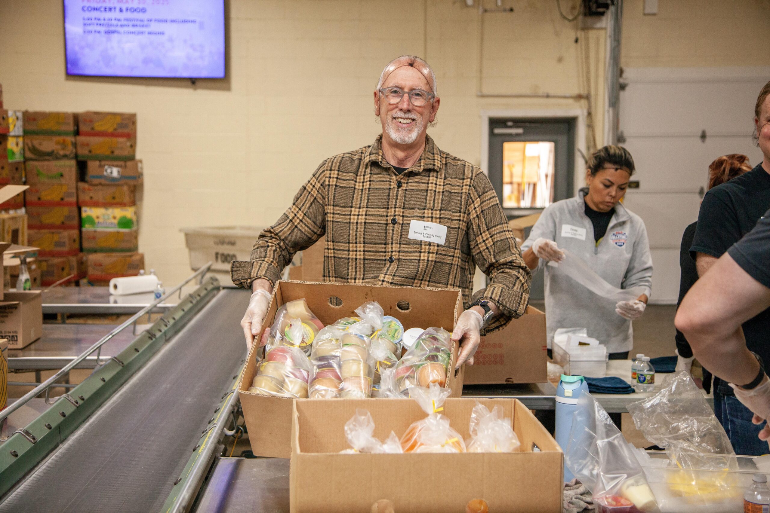 Volunteer distributing packaged food items in a community food bank, showcasing teamwork and community support in a warehouse setting.
