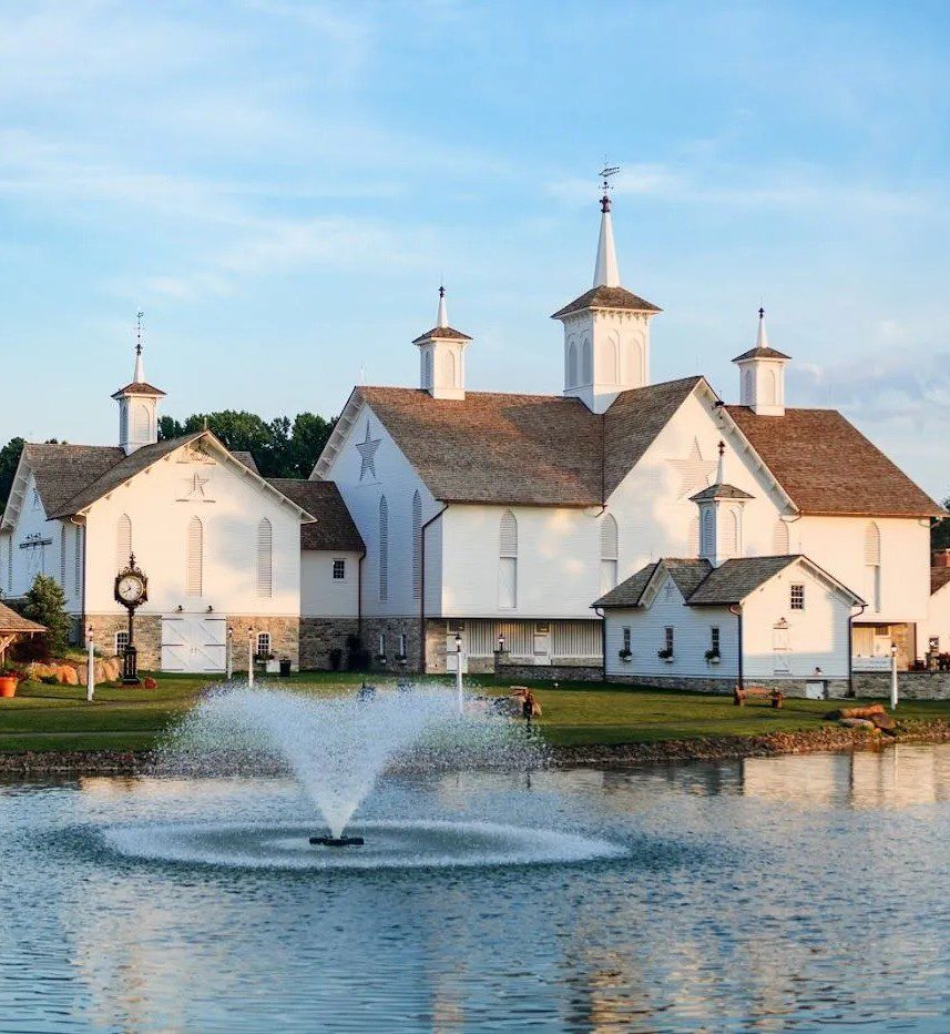 Historic white church with multiple spires and star motifs reflected in a serene pond, featuring a fountain and lush green surroundings. Ideal for showcasing architectural beauty and tranquil landscapes.
