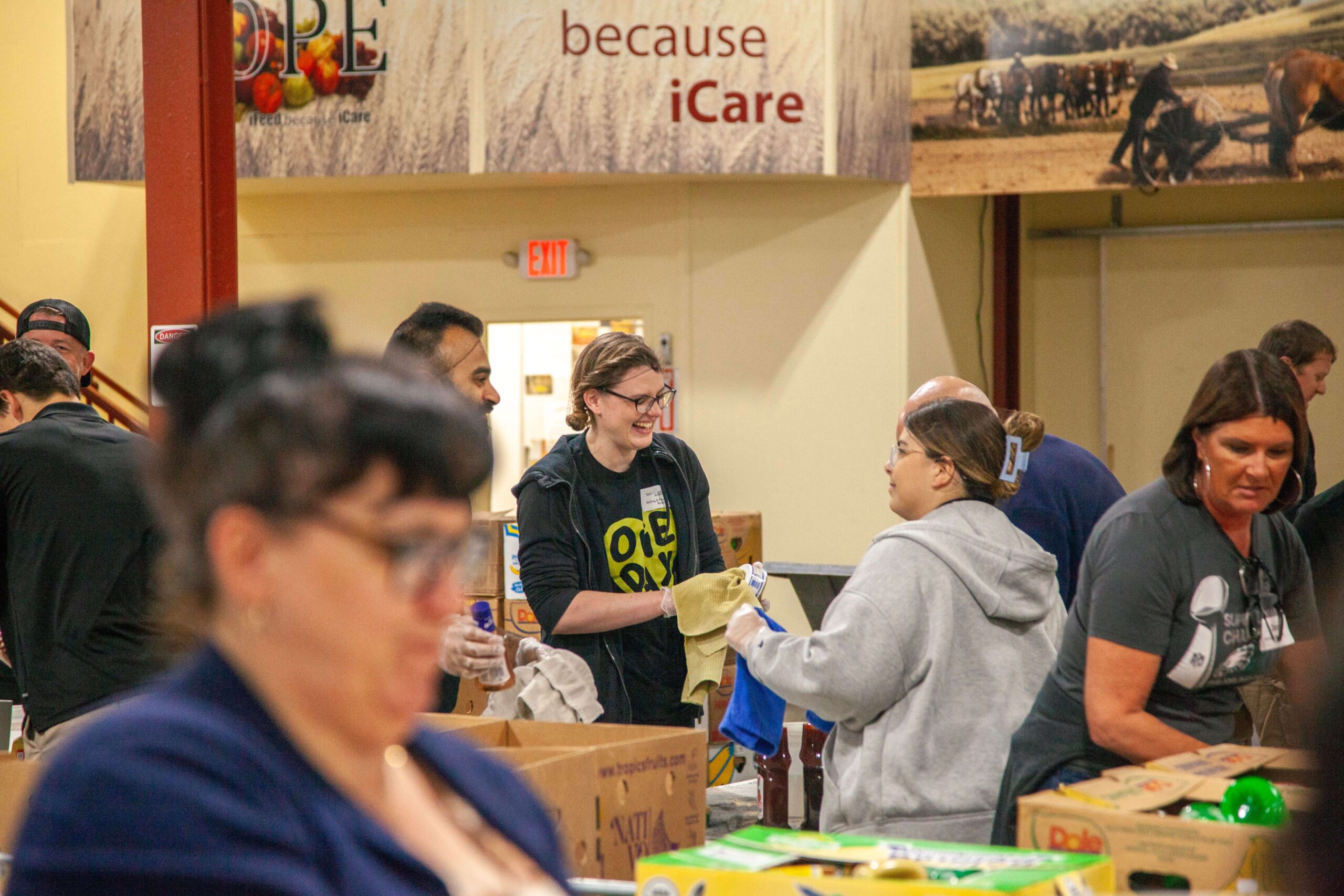 Volunteers sorting and distributing food at a community food bank, showcasing teamwork and support for those in need. The background features a banner emphasizing hope and care.