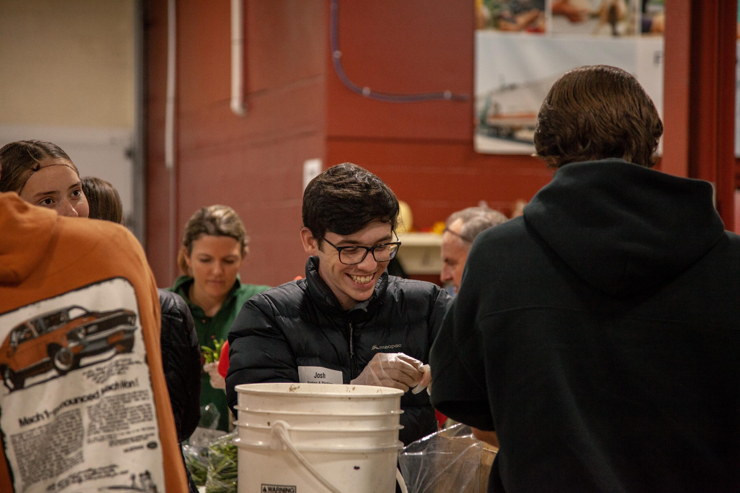 Volunteers participating in a community food distribution event, smiling and engaging while preparing fresh produce for local families. The setting features a warm, inviting atmosphere with a focus on teamwork and service.