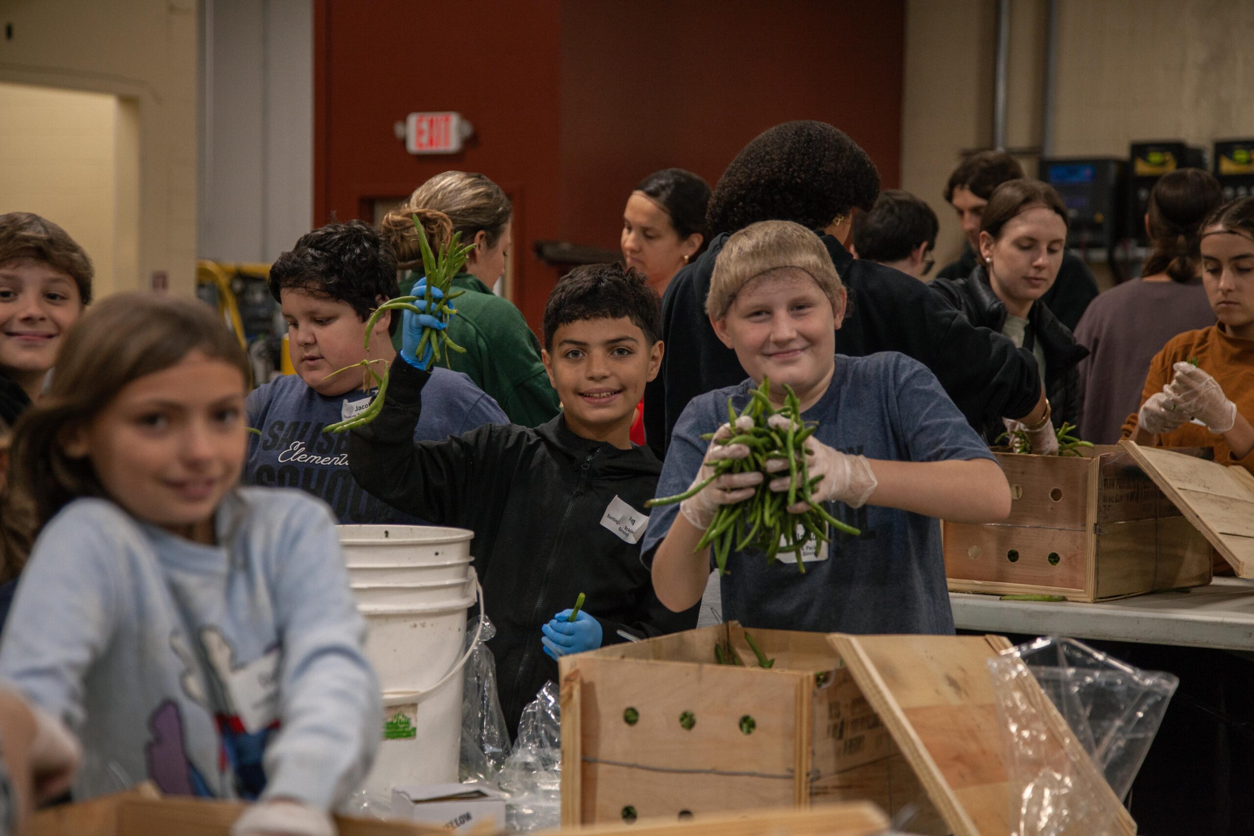 Children participating in a community service event, sorting and packing fresh vegetables in a warehouse setting, promoting teamwork and healthy eating.